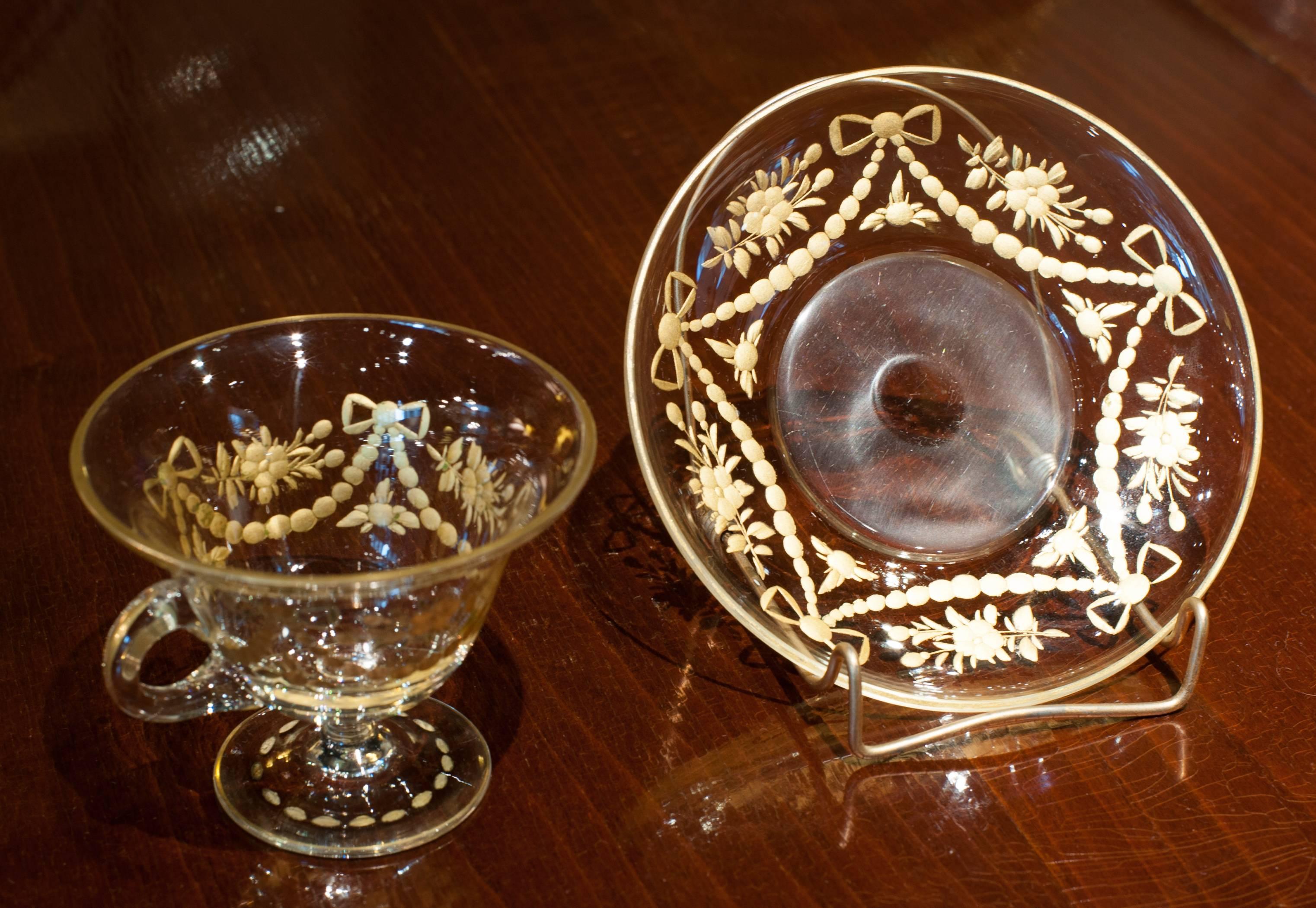 French glass punch cup and saucer with applied loop handle. The glass is hand engraved and gilt. The pattern on both pieces is swags tied with bows and flower clusters. The original use for this piece was probably for punch.

(This item is eligible