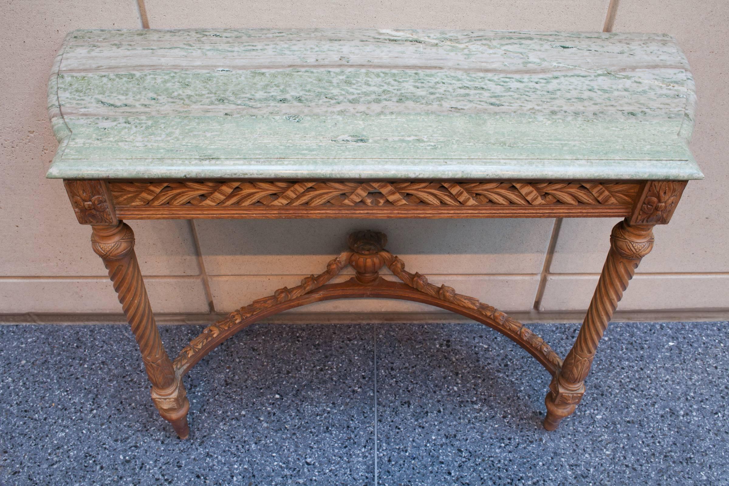 Carved wooden two-legged Louis XVI style console. The apron is carved to resemble ribbon wrapped leaves, while the legs are fluted spirals. The table is secured to the wall by two screws through the back apron. The shaped marble-top has an ogee edge