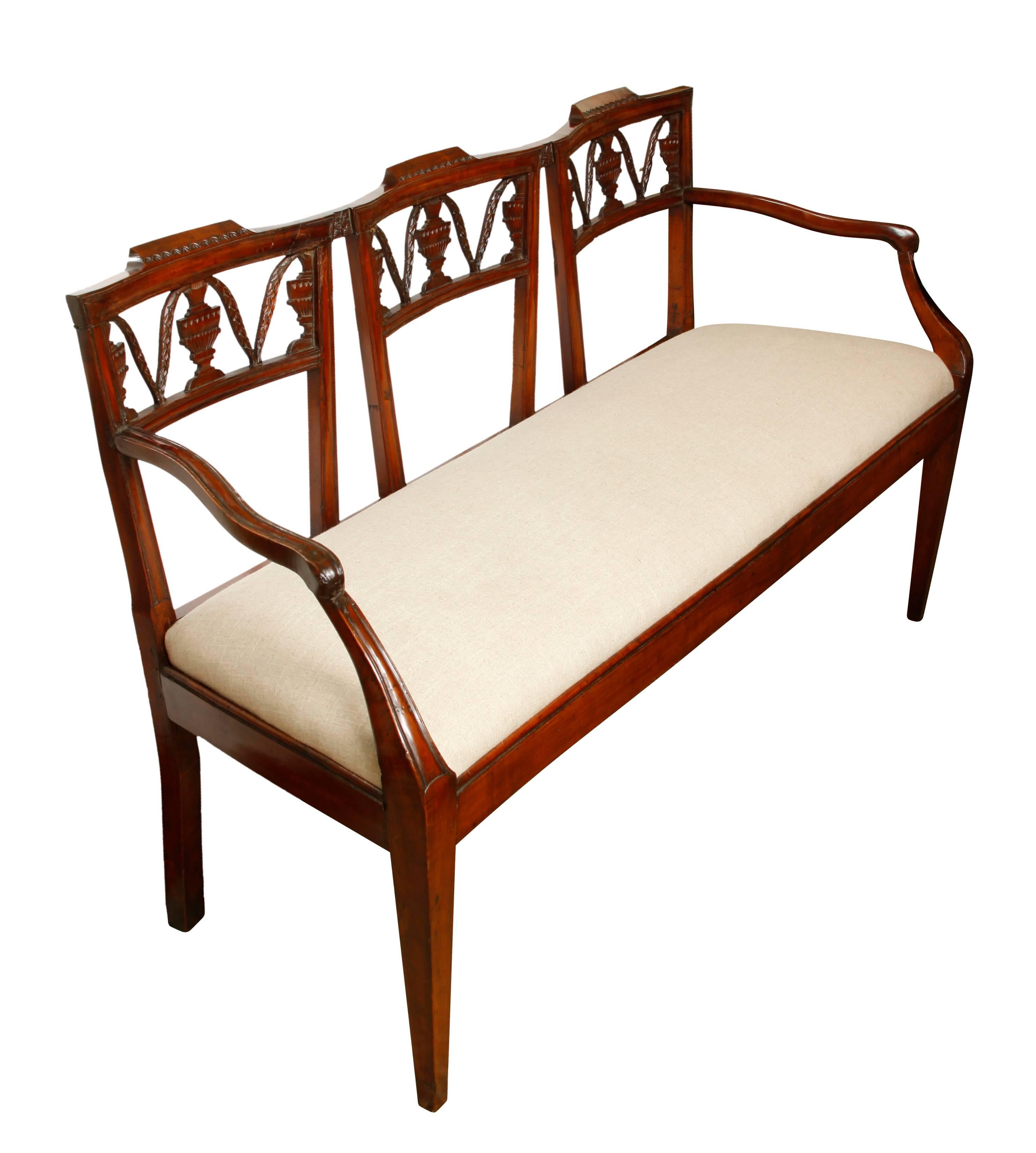 A mahogany hall bench of exceptional style and quality. The open back consists of three sections, beautifully decoration with hand-carved neoclassical details, and slightly curved at top. The arms have an elegant, slightly serpentine shape, and the