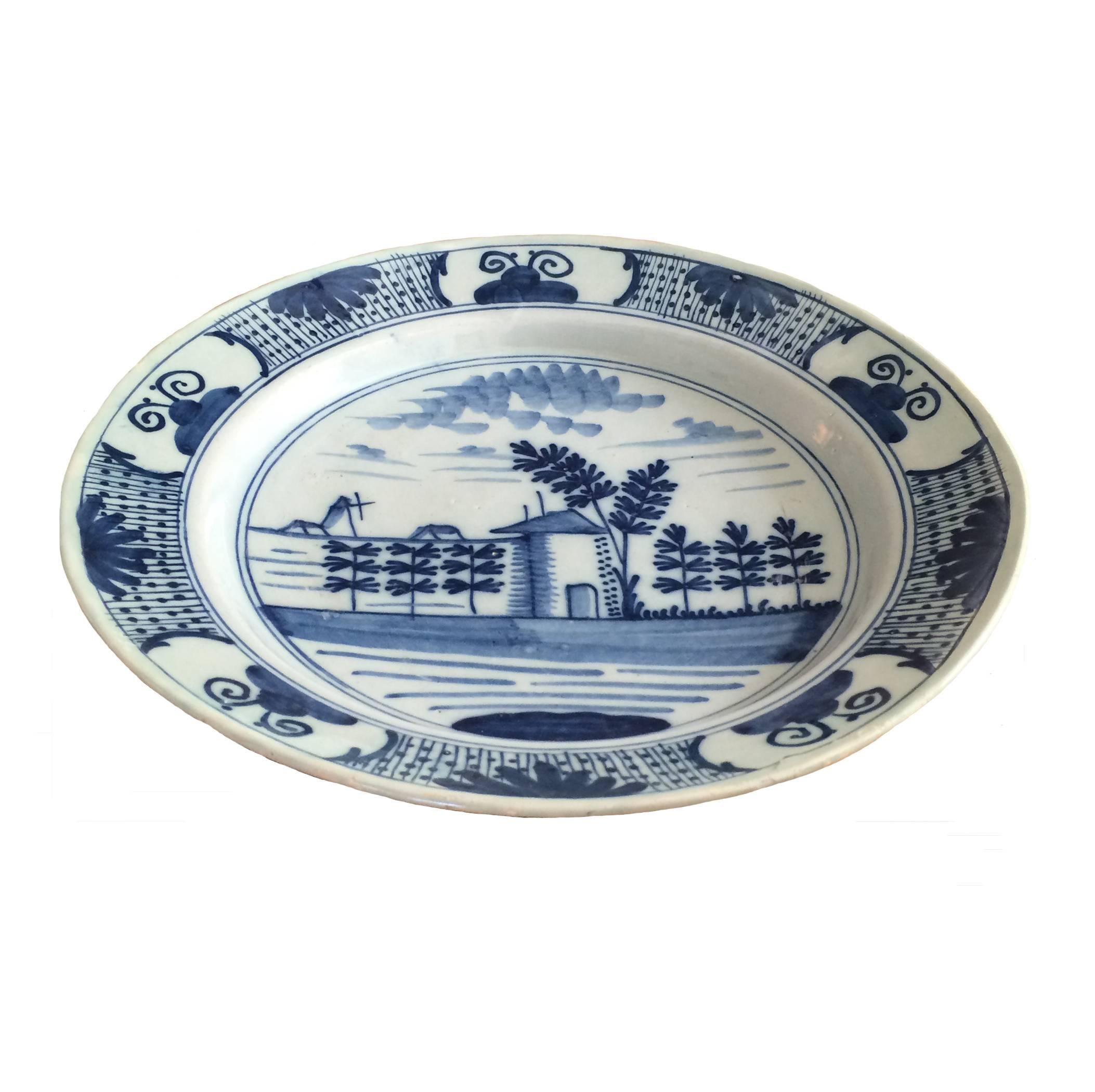 Large blue and white delft plate depicting a serene setting, a home surrounded by trees and water, 18th century.

