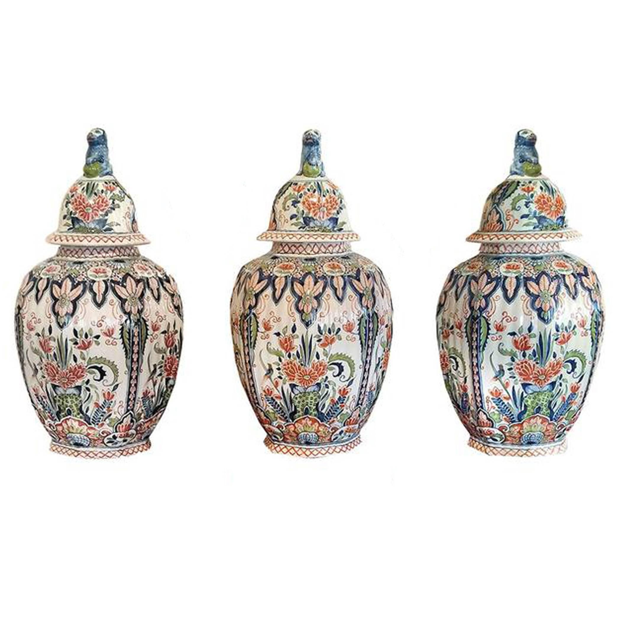 Five piece delft garniture set consisting of three lidded lobed urns; lids surmounted with regal lions in repose; two octagonal tapered lobed vases. Blue, red and green predominantly; series of medallions, flowers, geometric borders; 19th century.