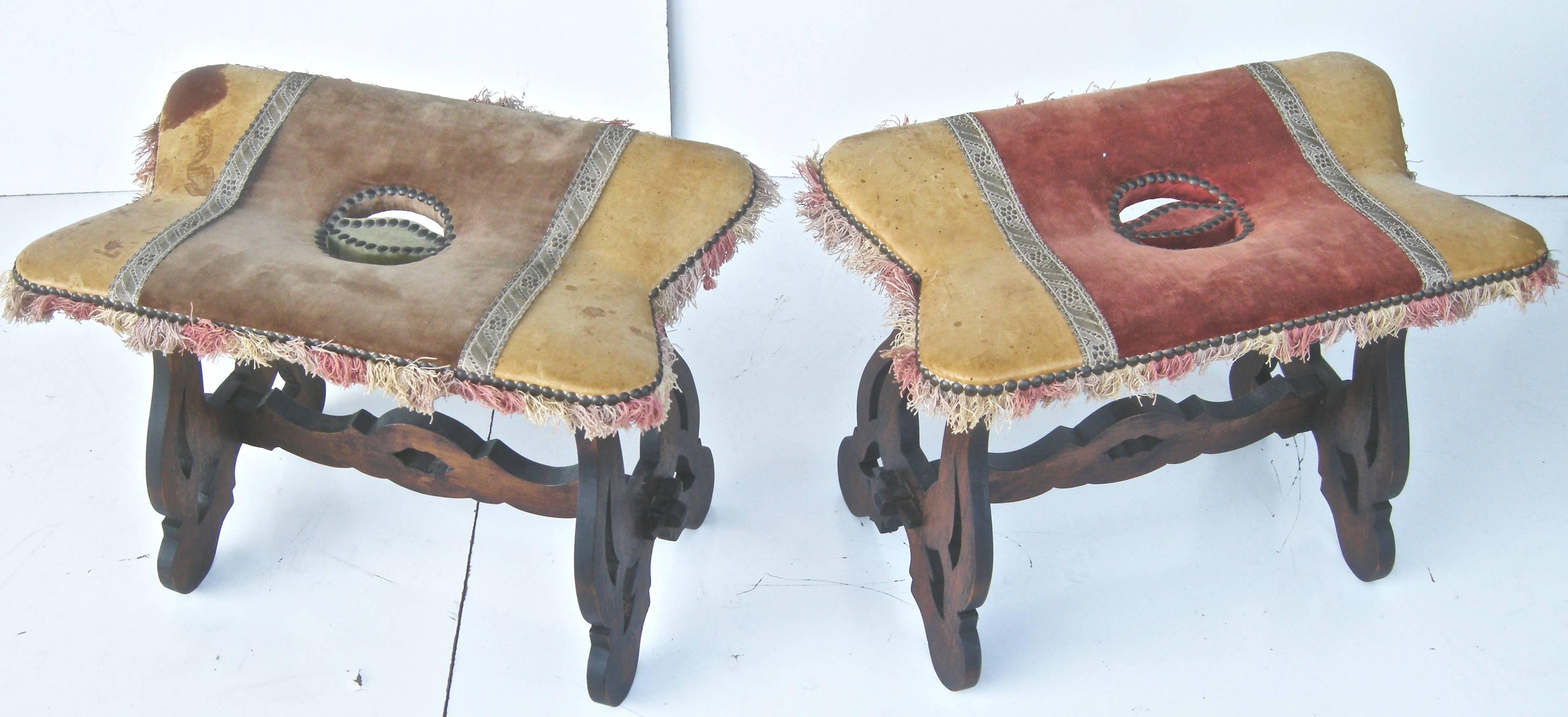 Handsome pair of, vintage, petite, Spanish foot stools, having semi-rustic, continental style and designs. Original leather and fabric combination tops with heavy studding and fringe accents. Warm finishes with some fabric staining and