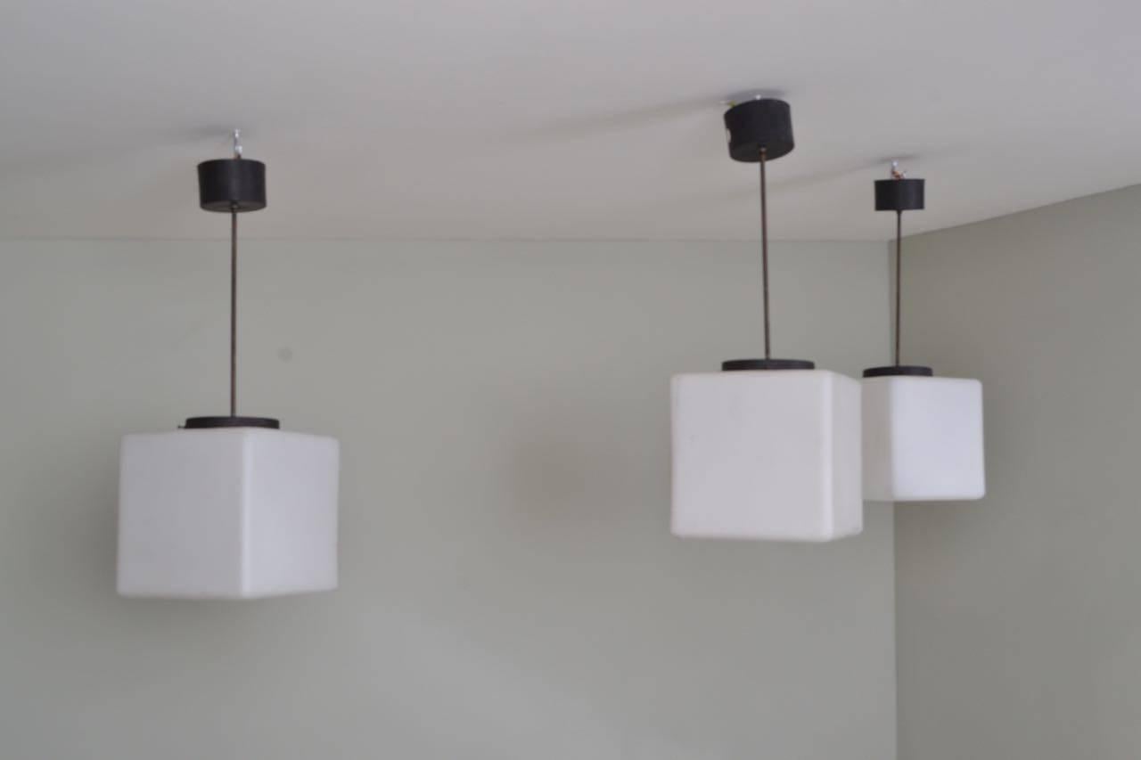 Set of three black painted iron and square opaline glass pendant lamps.