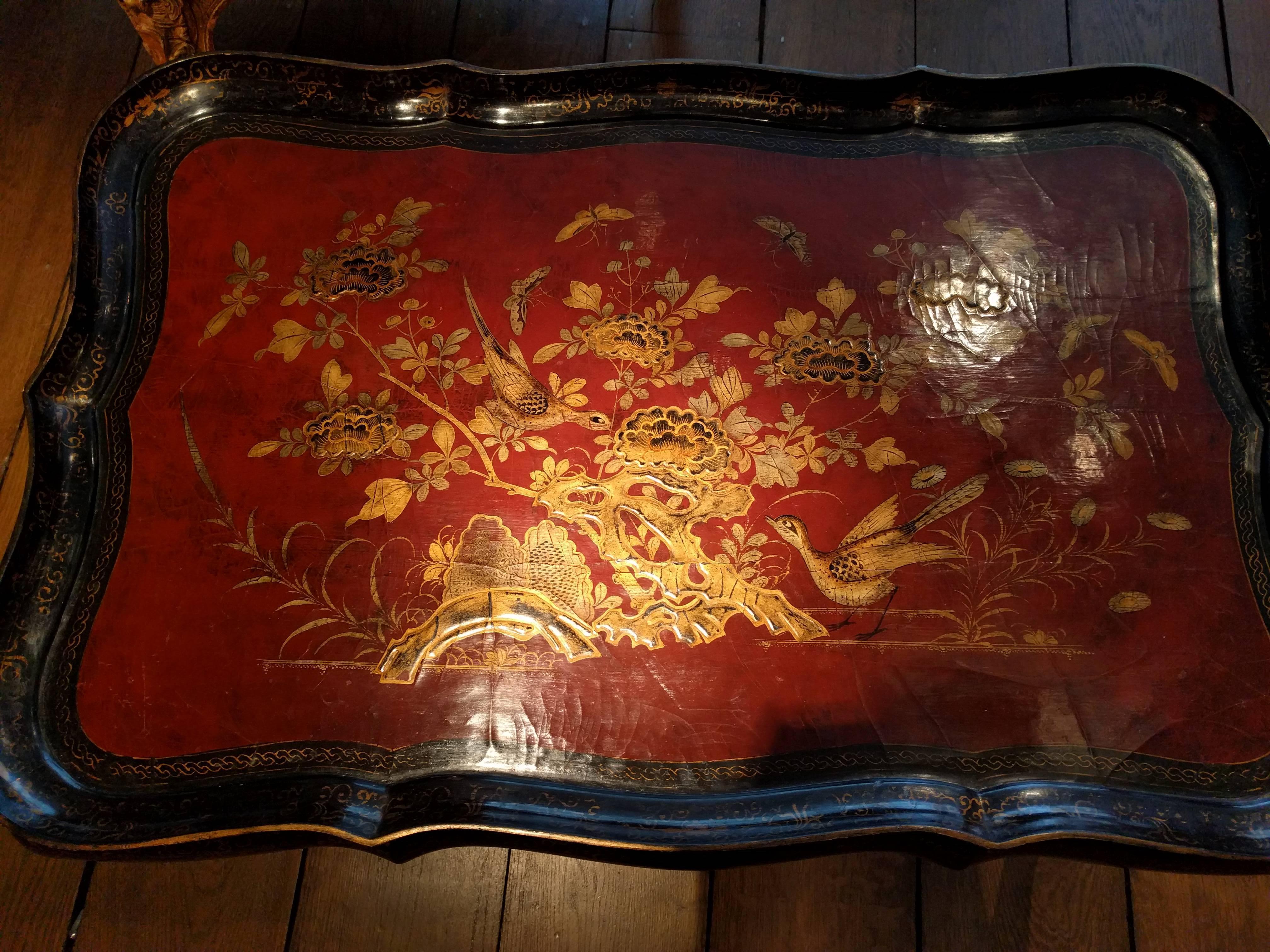 French chinoiserie lacquer tray table by Maison Jansen, circa 1950. The removable red ground top depicting a riverscape with birds, butterflies and oversized chrysanthemums with gilt with black detailing. The tray with a black serpentine border