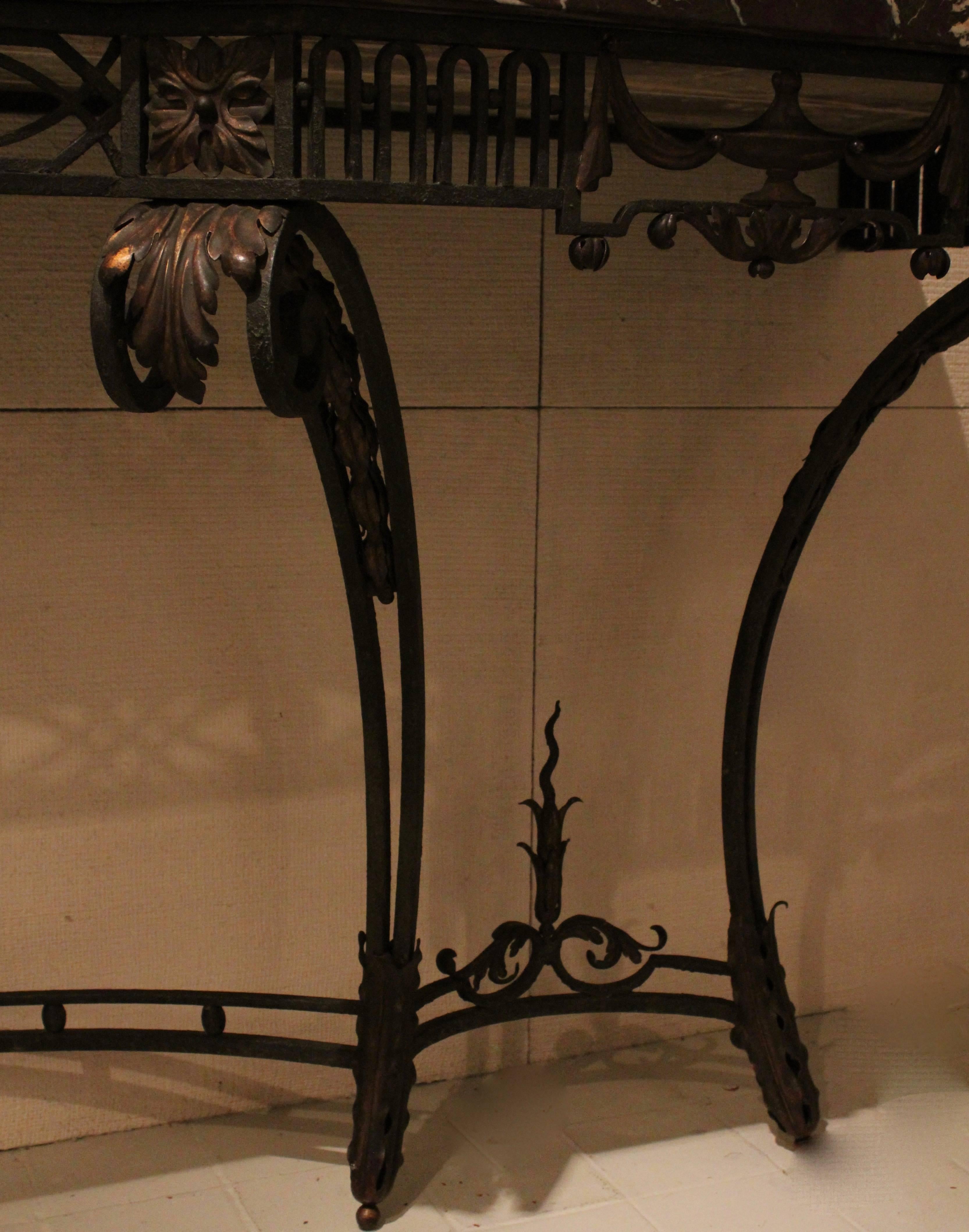 An elegant wrought iron neoclassical, console table with a shaped campana marble top France, circa 1900. The beautiful shaped banded campana marble top sits above a stylised frieze, which features gilt urns with swags on either sides and four gilt