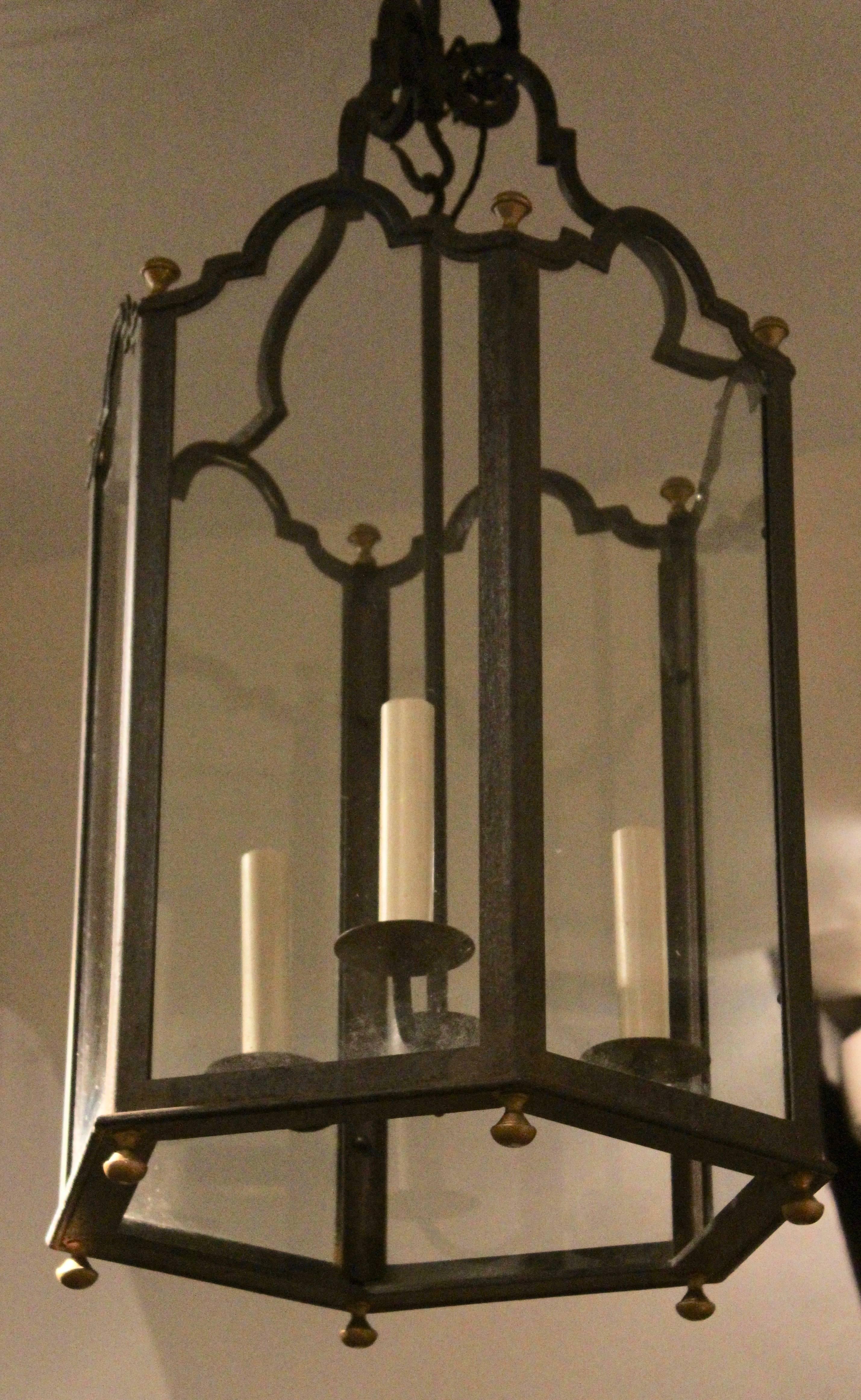 Pair of French hexagonal wrought iron lanterns, circa 1930. Each glass pane with a simple wrought iron frame finished with a stepped arch top. Each corner, top and bottom punctuate with polished brass finials at the corner of each point. Four