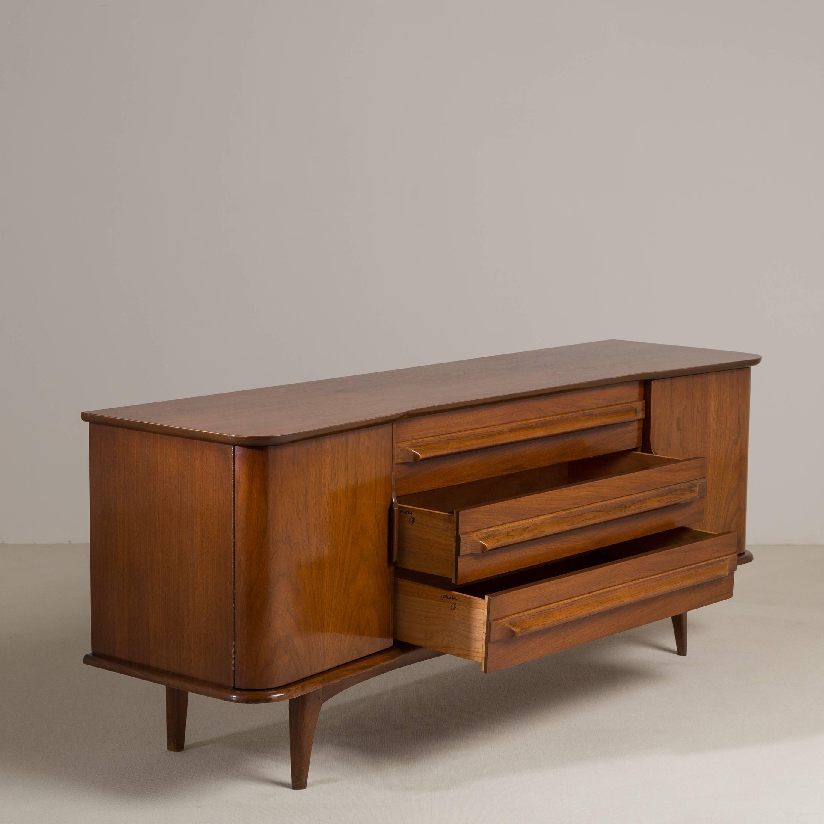An Elegant American Mid Century Modern Walnut Cabinet featuring Twin Doors concealing Drawers, and Three External Drawers with Carved Wooden Handles circa 1960s