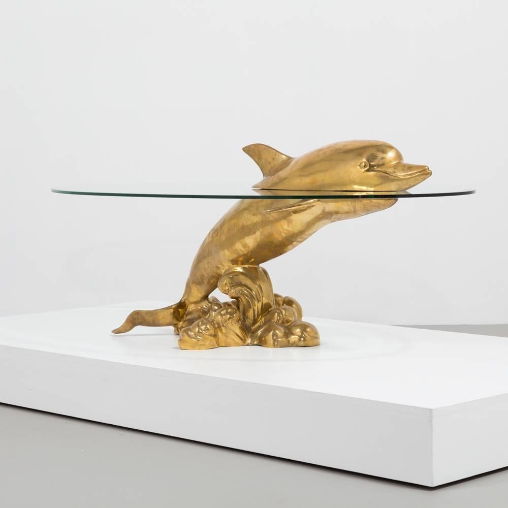 A polished brass and glass coffee table depicting a bottle-nose dolphin propelling through water, 1960s
