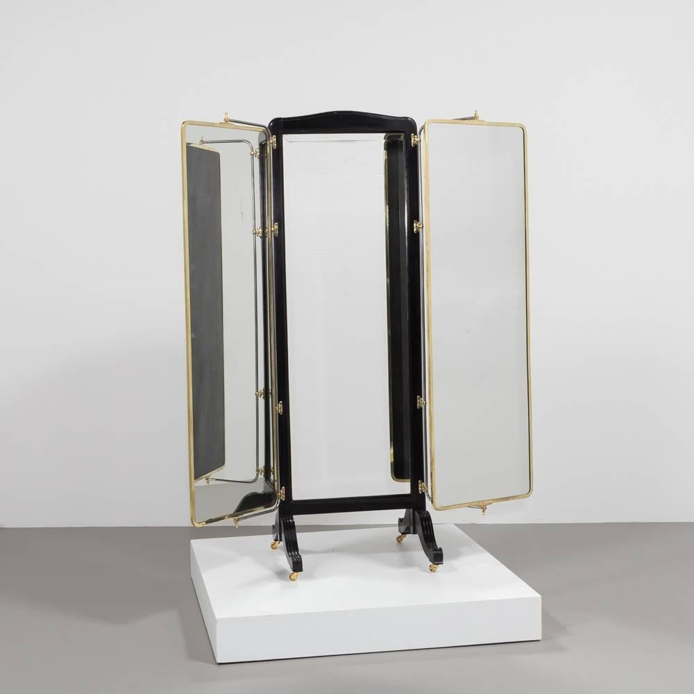 A French brass and ebonised wood framed three fold mirrored dressing screen set on castors, circa 1890.
Two brass framed mirrors which pivot independently fold out from an ebonised wooden framed mirror. The backs of the mirrors are ebonised wood