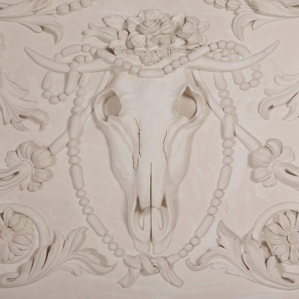 A large neoclassical style plaster panel with an ox skull surrounded by flora and fauna and a plaster moulded frame


