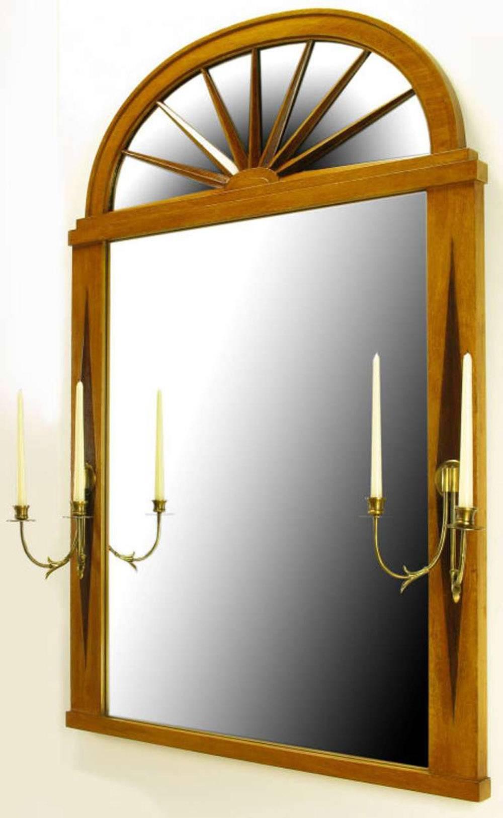Grosfeld House Empire style mirror with arched top carved wood sunburst over mirror. Framed in bleached mahogany with contrasting dark walnut diamond shape inlay. At the middle of each diamond is a two-arm brass candelabra sconce.

Sconces extend