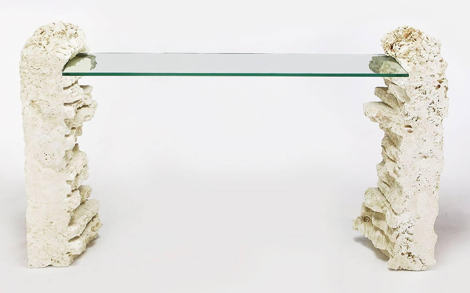 Natural rough-hewn fossilized coral stone pillars cut to form an organic piece of furniture. This console table consists of fossilized coral stone that has been scored and unfinished to give the appearance of found pieces. The glass top is 12