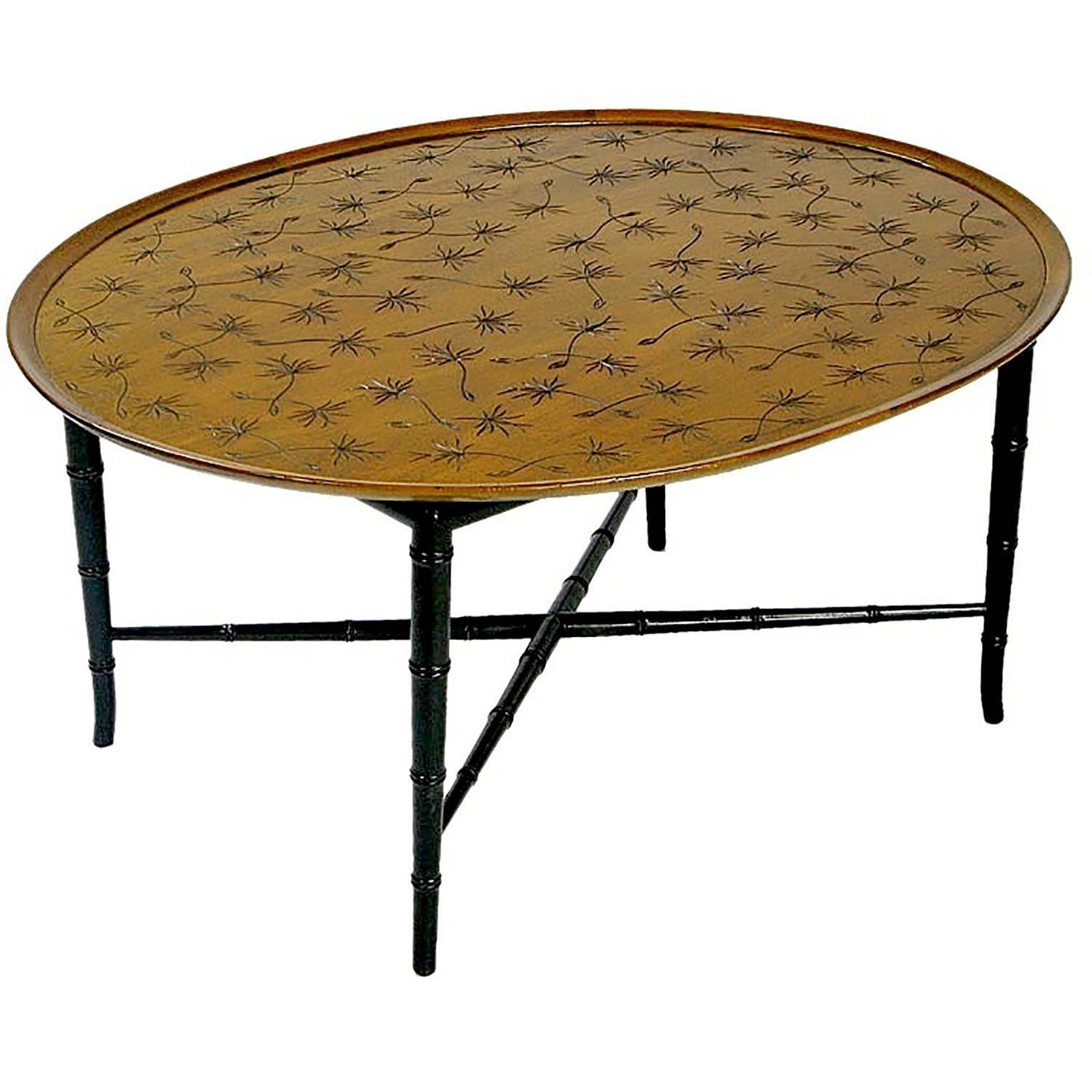 An elegant oval mahogany coffee table by Kittinger. The raised edge surrounds a flat center surface into which airborne thistle seeds have been carved in sunken relief. The top is supported by ebonized bamboo form legs, connected with an X stretcher.