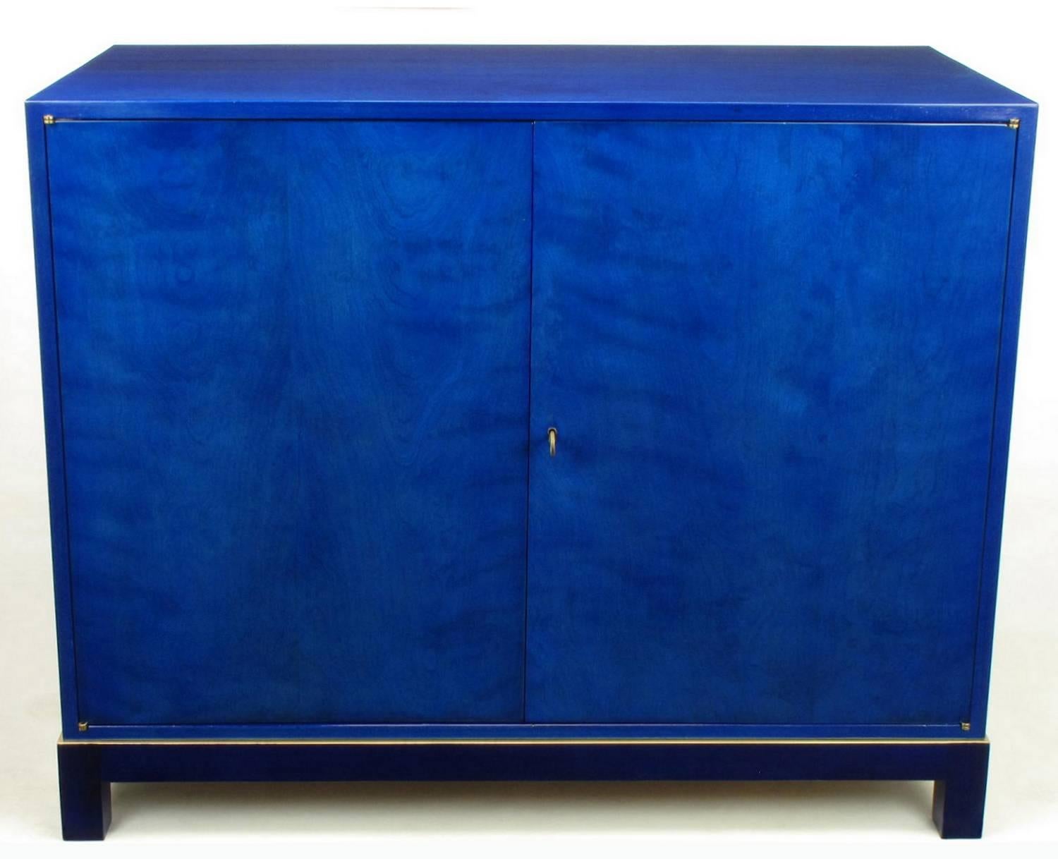 Pair of restored early Baker Furniture sideboard cabinets dyed a beautiful lapis lazuli blue with parcel-gilt midnight blue bases. One cabinet features fourteen lined drawers for flatware. The other cabinet contains a pair of shelves for hollow