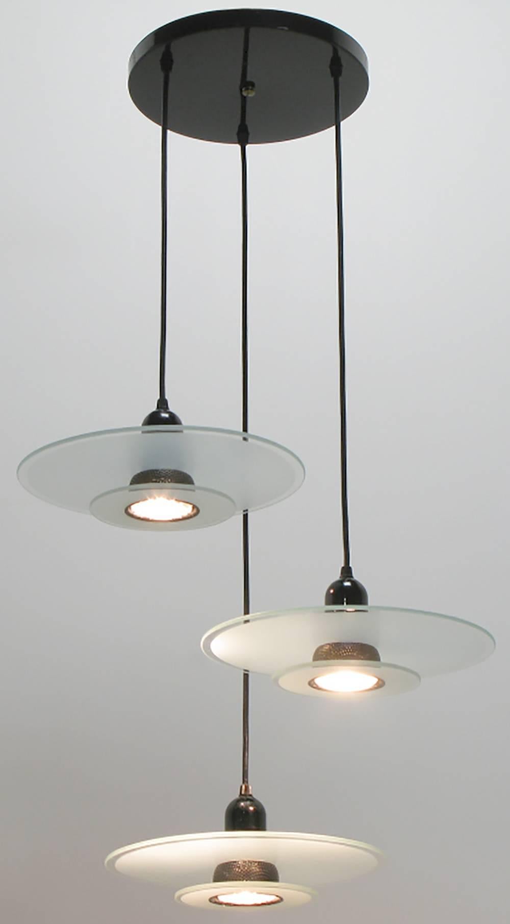 Art Deco revival three-light pendant fixture with etched and clear two part glass disc shades. Black enamel steel bullet housing is pierced between the 1st and second glass discs. Black wrapped lighting cable suspends each fixture from the black