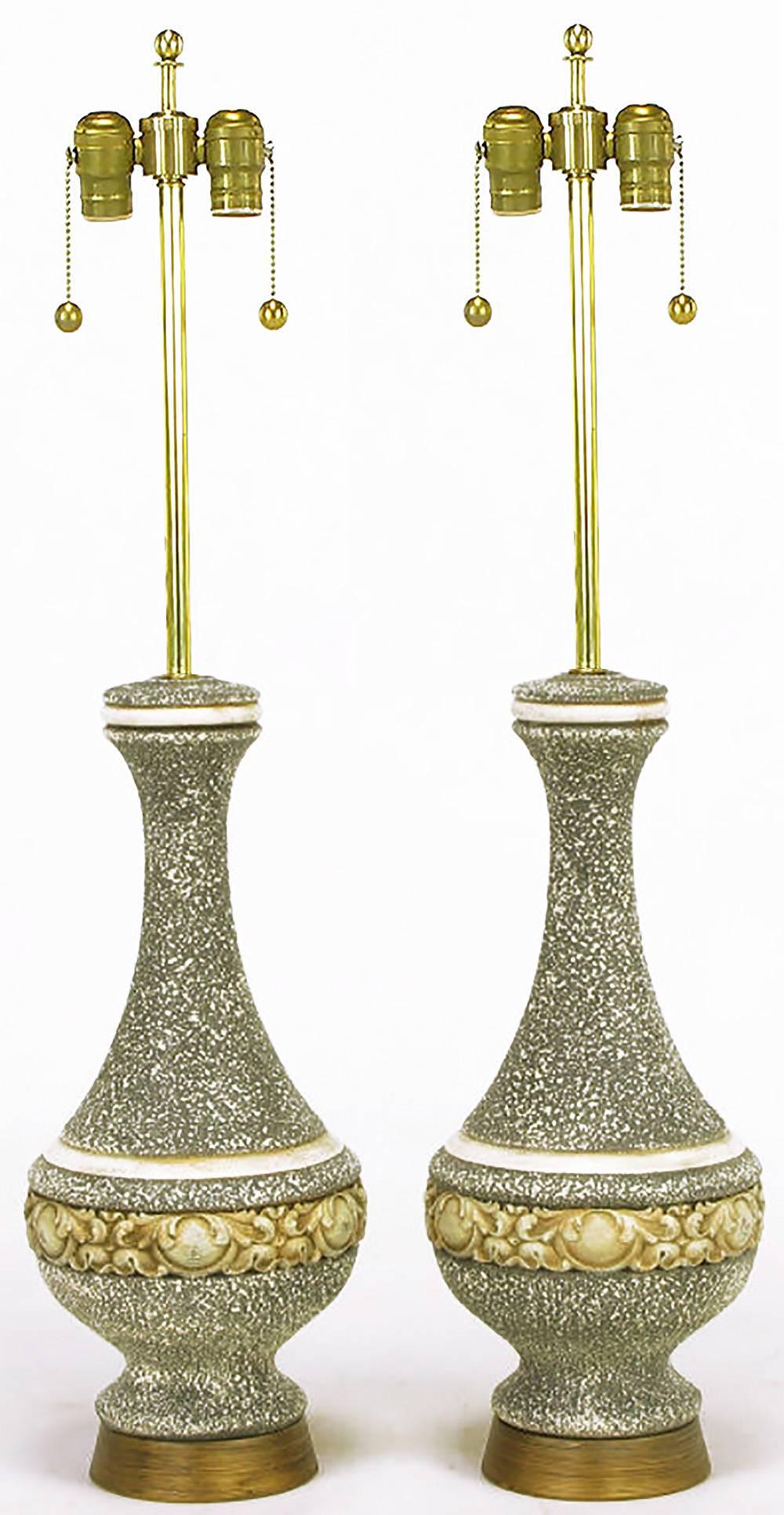Pair of urn form Rococo style heavy cast plaster table lamps with a tactile variegated gray glaze and aged gilt finish. Antiqued brass bases with brass stems, harps and sockets.