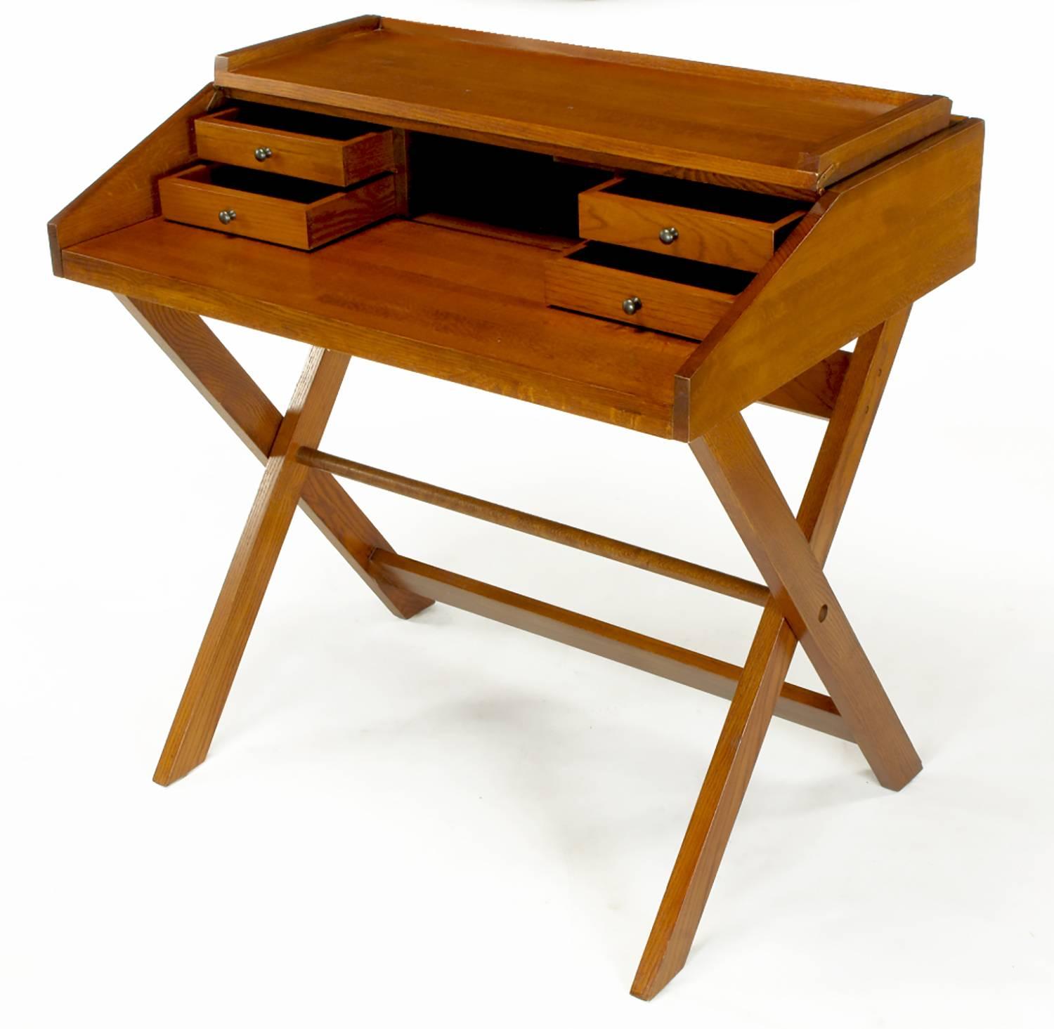 Flip-Top-Schreibtisch aus Eschenholz in Thekenhöhe in Färbertönen mit eingeschnittenen Rückwänden. X-förmiger, zusammenklappbarer Sockel mit Fußleiste. Die abgeschrägte Oberseite lässt sich hochklappen und gibt den Blick auf vier zierliche
