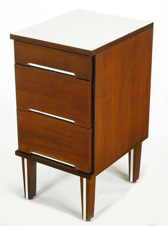 Three drawer walnut nightstand with recessed white lacquer drawer pull openings. Tapered solid walnut legs with white lacquered incision. White micarta top. Similar to designs offered by Herman Miller. See our listings for the matching three drawer