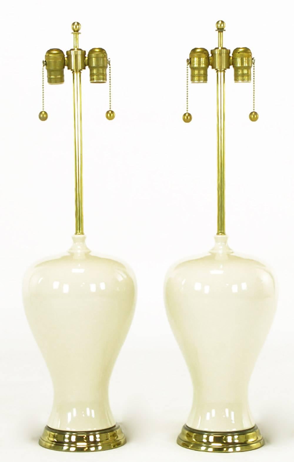Pair of voluptuous ivory glazed ceramic table lamps with patinated brass finished bases. Organic form moves seamlessly from base through the ivory ceramic body to the brass stem and double socket cluster. Sold sans shades.
