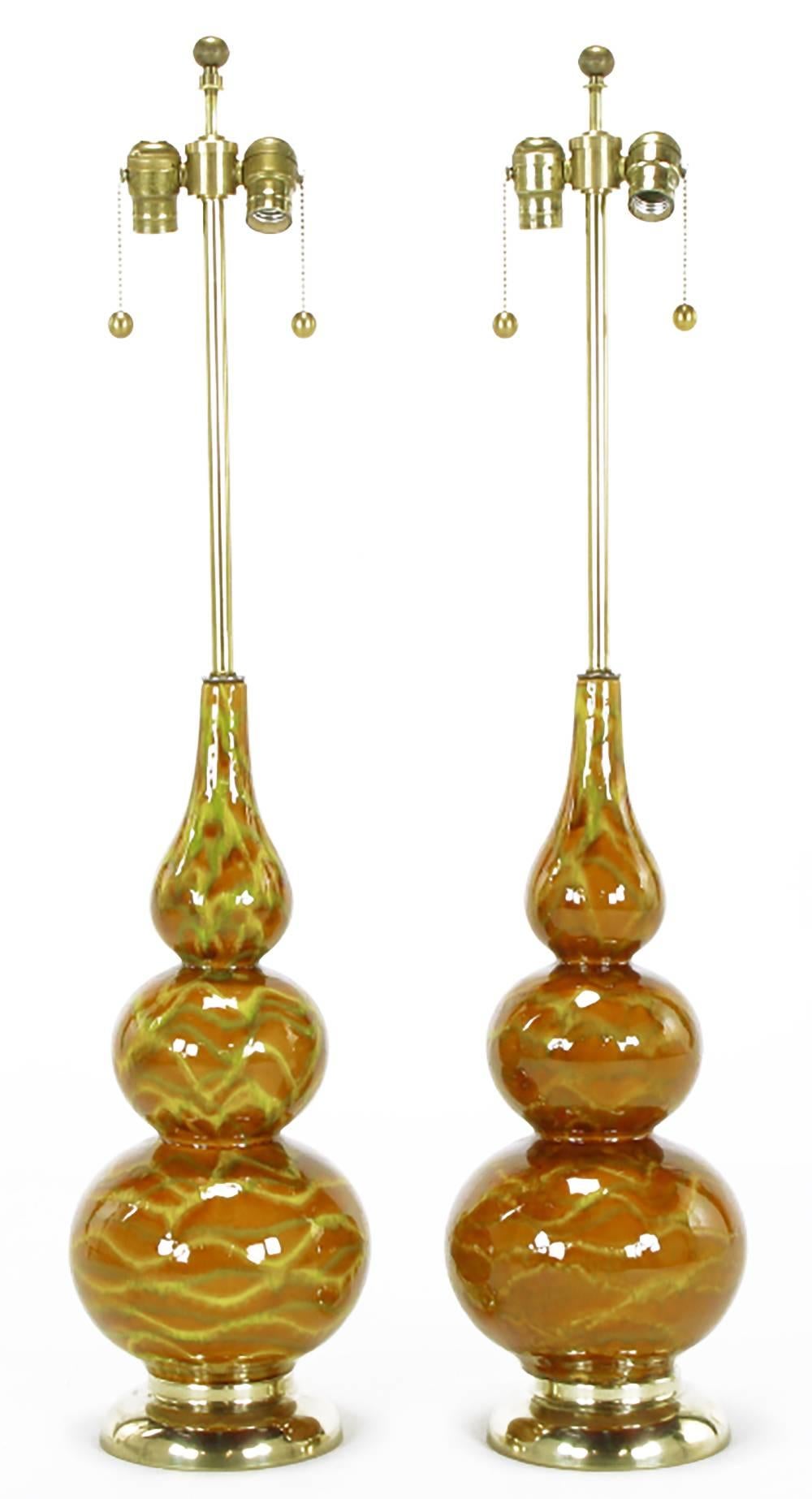 Pair of caramel glazed ceramic triple gourd form table lamps with saffron yellow and olive green wave form striping. Brass base and stem with double cluster sockets, sold sans shades. One lamp has more prominent striping than the other. Sold sans