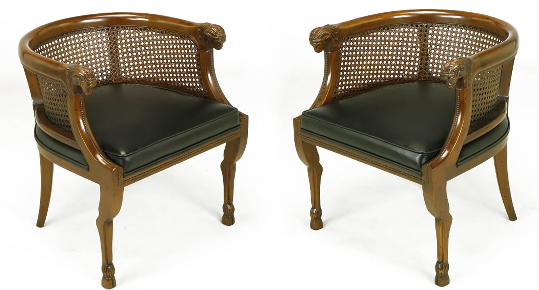 Empire style barrel back armchairs by Tomlinson. Each chair has a pair of hand-carved ram's heads at the peak of the front legs which are dramatically shaped similar to actual ram hind legs with hooves as feet. New Spinneybeck black leather seats