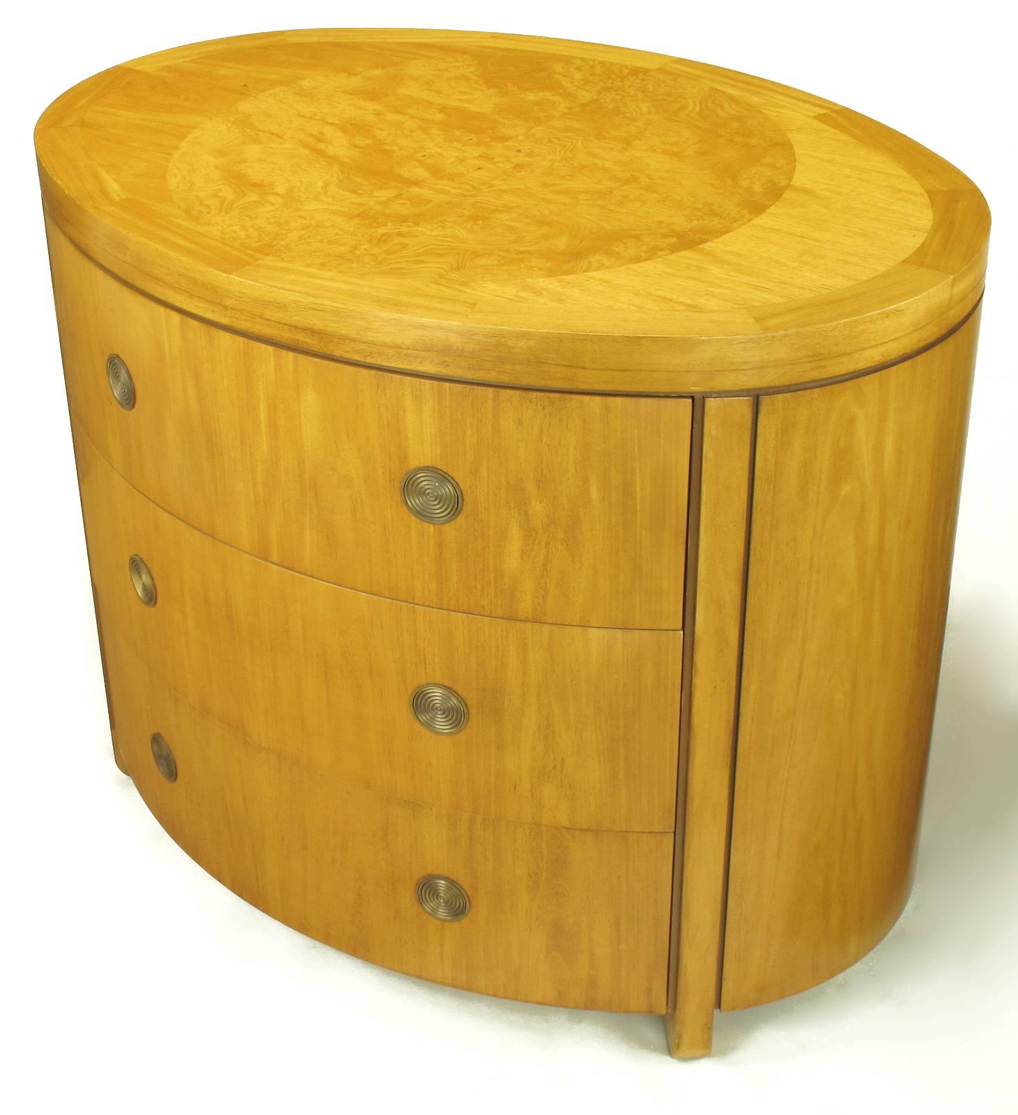 Charles Pfister for Baker Furniture oval three drawer commode. Prima vera mahogany case and drawer fronts with flush concentric circled swiveling brass pulls. Four radius end legs and olive ash burled parquetry top are set off from the case by