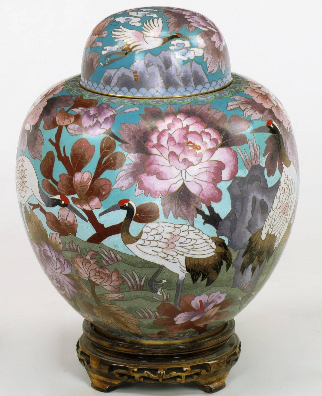 Pair of Chinese cloisonné capped urns with carved and pierced fruitwood bases. Red-crowned cranes with assorted flora on a sky blue background with volcanoes and muted green mountains. Most probably made by Jingfa, award winning manufacturer of fine
