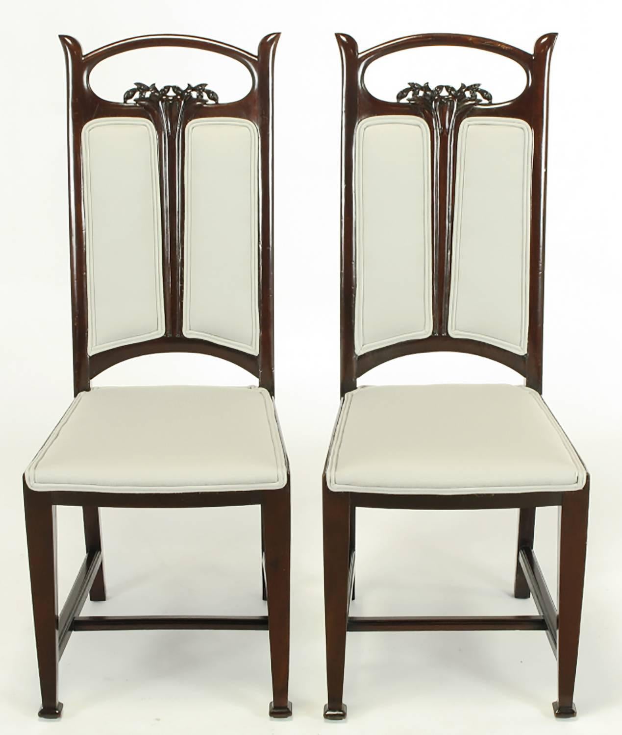 Pair of side chairs with Arts and Crafts and Art Nouveau influences. Mahogany frame with split back and center Art Nouveau carved floral detail and open elliptical top. Arts and crafts inspired legs with carved front feet and H-stretcher with slight