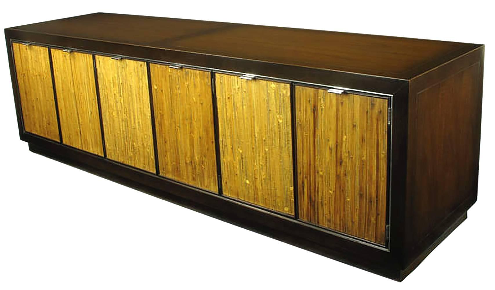Dark walnut low cabinet with grass cloth inlaid doors in the manner of Harvey Probber. Double doors open to reveal an illuminated center section, right and left sections feature black leather like covered drawers. Finished on all sides with incised