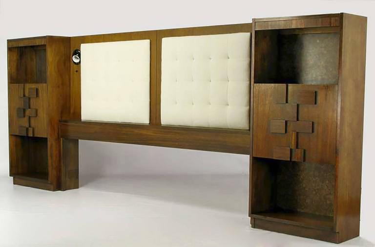 Walnut wood headboard for a king bed, with matching and integral patchwork wood relief drop door nightstands. Two upholstered panels are biscuit tufted with ivory textured cotton fabric. Three section even height night tables have upper and lower