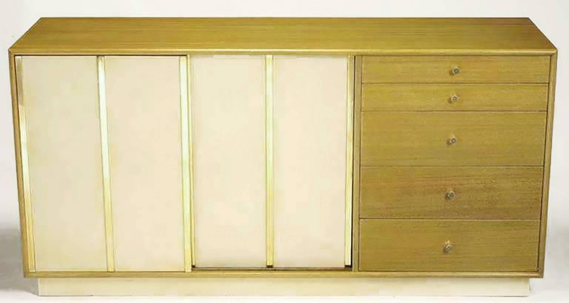 Harvey Probber bleached mahogany long dresser with ivory leather-clad sliding doors and plinth base. Three brass flat bars detail each leather door, giving the appearance of four sections. Behind sliding doors are four additional drawers and three