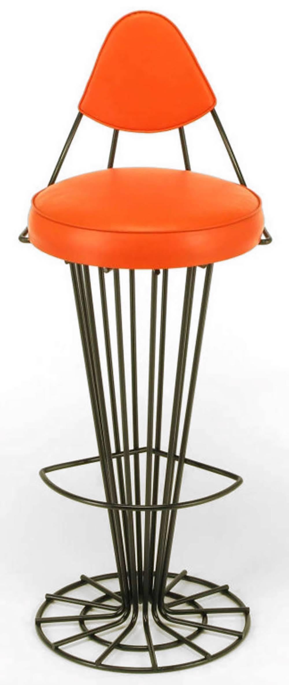 Refinished in a black satin enamel, these unusual iron bar stools consist of skeletal conical pedestals that open to a double ringed open circular base with a curved foot rest. Sculptural back rest in black satin iron and persimmon vinyl, persimmon