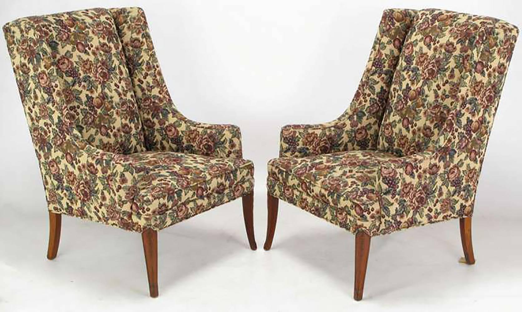 Pair of circa 1940s low arm wing chairs upholstered in a fruit and foliage tapestry. Mahogany saber legs have a lightly carved detail. In a similar style to early Grosfeld House with low turned arms and exaggerated rake to the chair back.