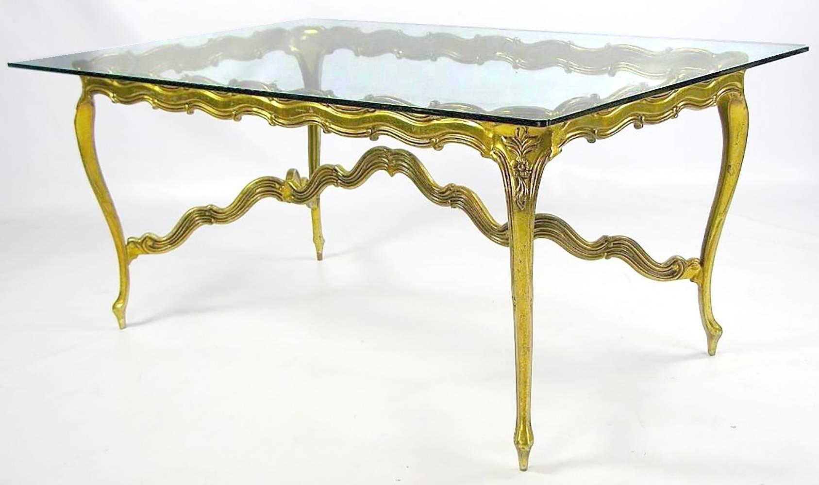 In a stylized Louis XV design, this table is a Mid-Century interpretation of a traditional form. The cast and patinated gilt aluminium frame is strong for its svelte profile, so it is visually lighter than its wood counterparts, with the clear glass
