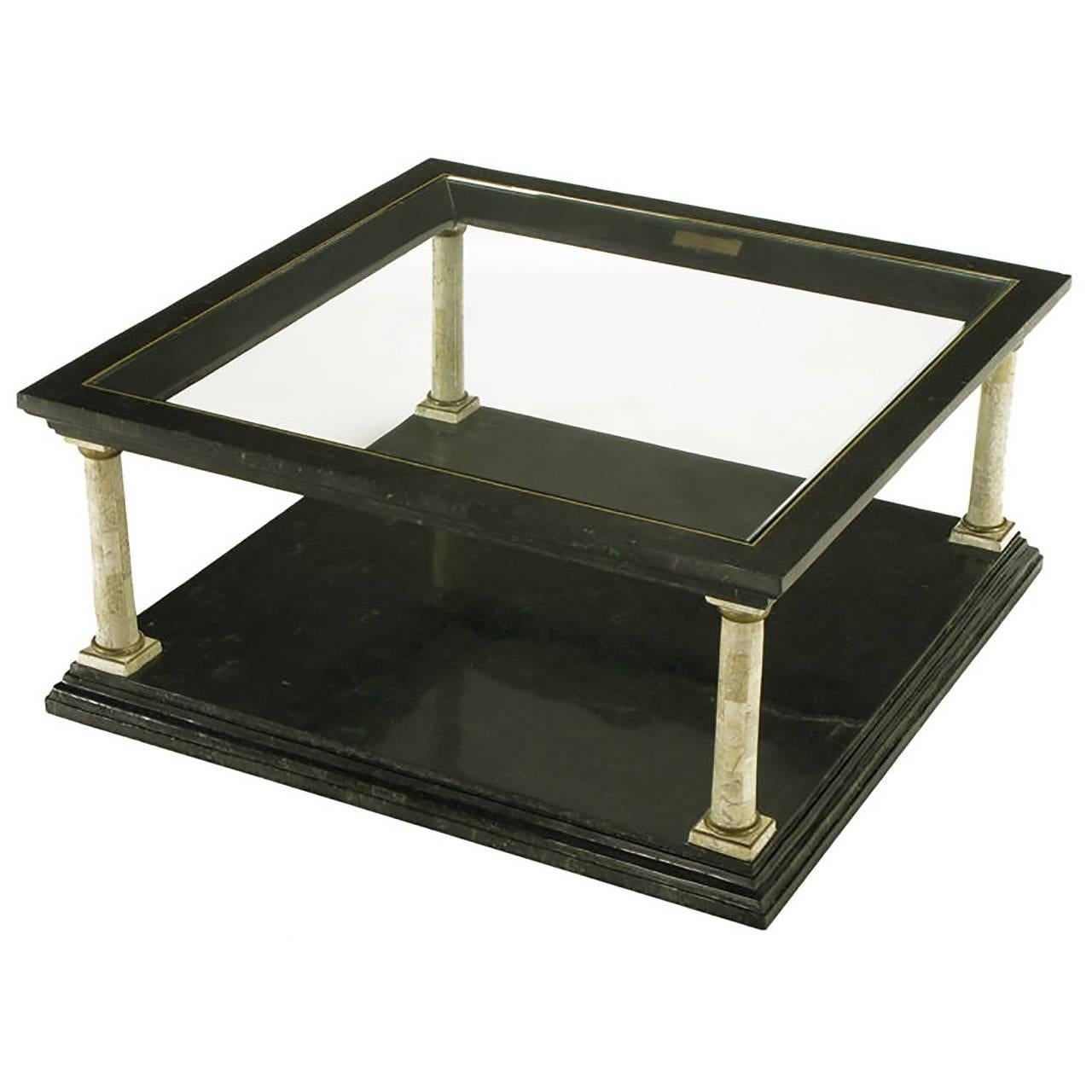 Features four Doric columns, with shafts of creamy tessellated fossil stone, atop a black tessellated marble base. The columns, with brass capitals and base rings, support the upper part of the table, which is also black stone. It has brass trim