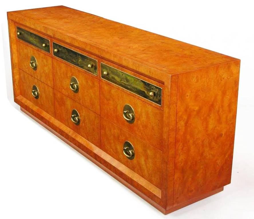 Beautifully burled chest, toned in a custom burnt orange lacquer atop a wood plinth. Nine drawers; three with acid-etched panels by Bernhard Rohne, accented by spherical pulls. Six with Asian drop bail pulls, backed by oval brass plates.

 