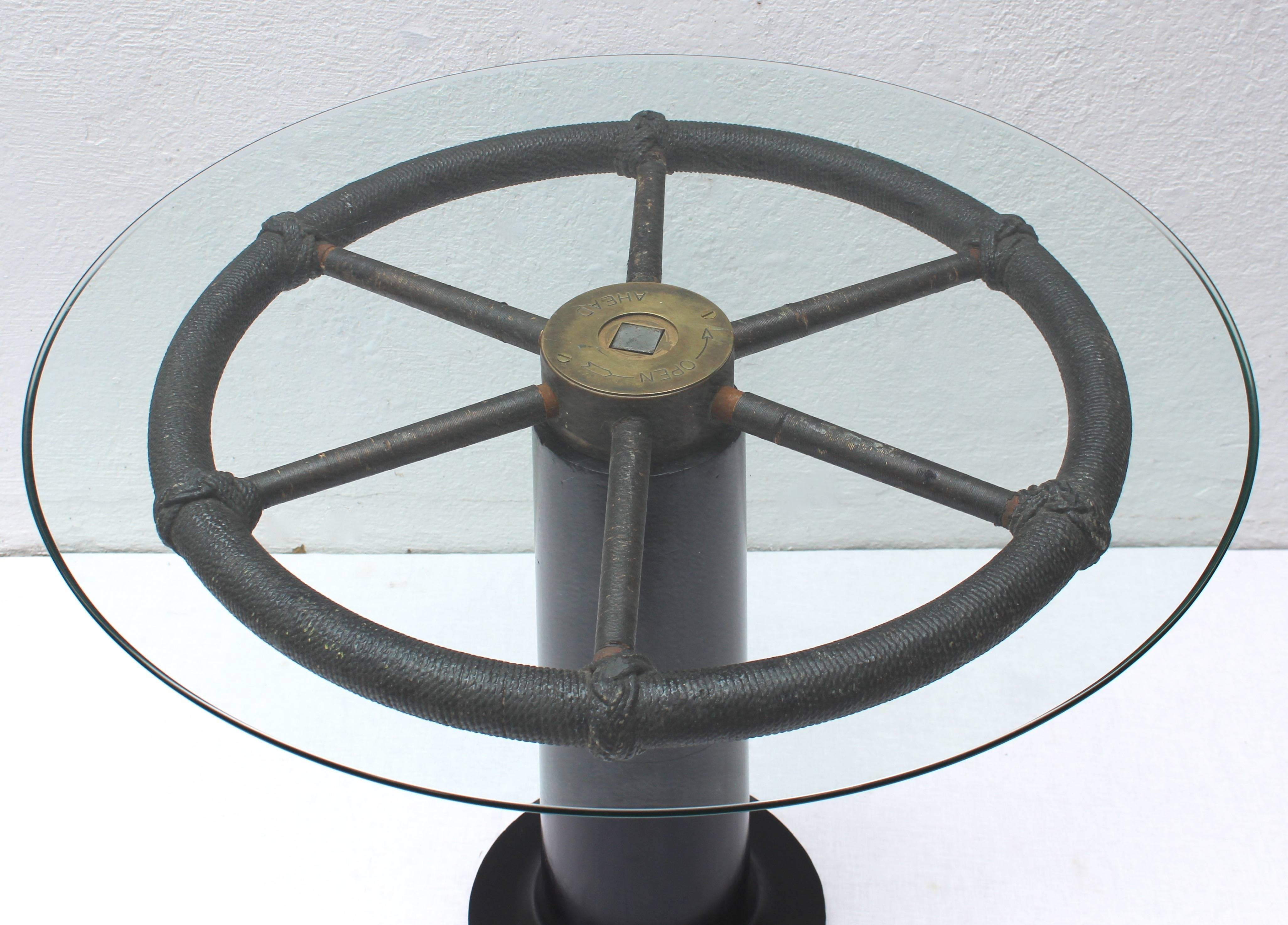 Wonderful and unique nautical table created with authentic ship's wheel mounted on ebonized wood pedestal base with a glass top.