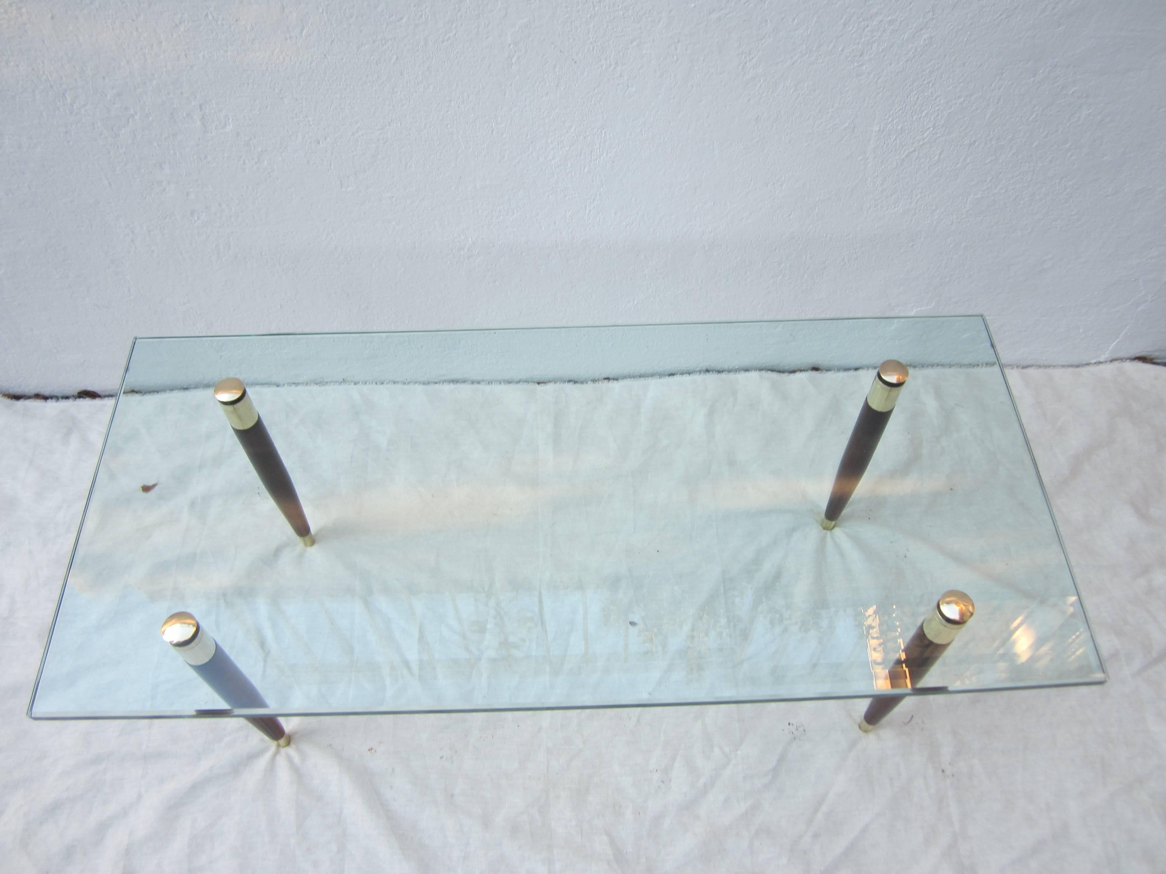 Elegant glass coffee table with brass and mahogany legs that sandwich the glass with brass caps on top. Great looking minimalism. Small chip to glass on underside in the corner, barely visible (see last picture).