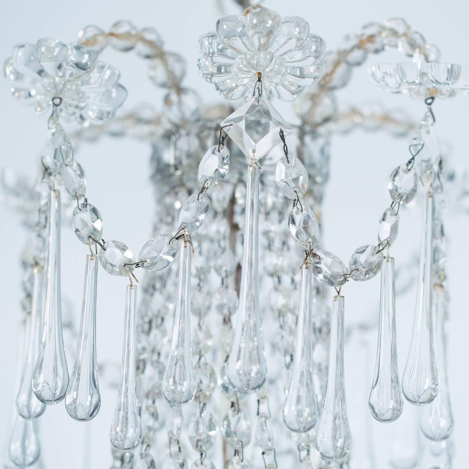 This elegant chandelier features a series of long crystal drops punctuated by crystal rosettes, framing the central cascading basket with its core of three lights. The drops are repeated around the top and bottom. Each crystal in this piece, is