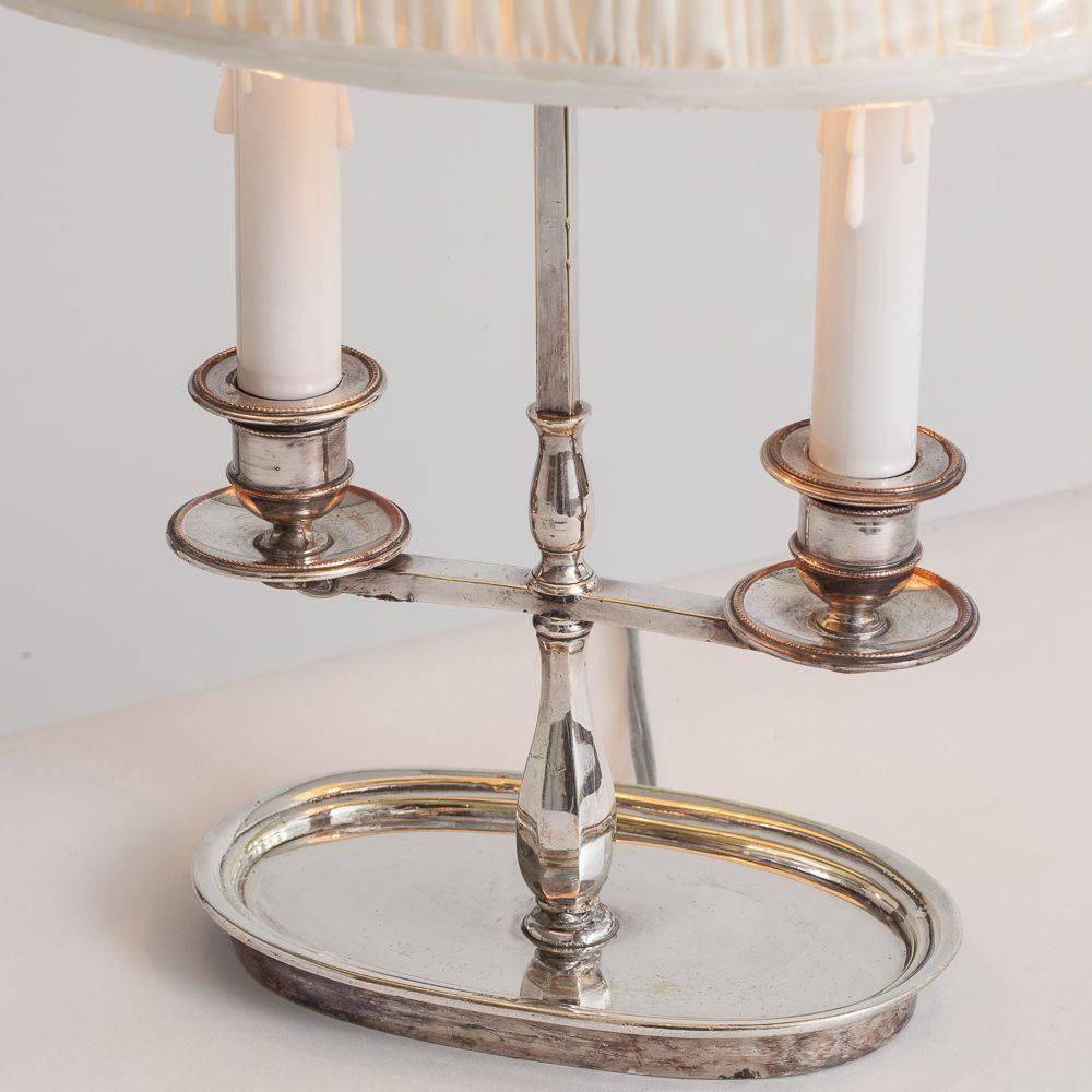 This adjustable silver plate lamp has two lights and is perfect for a desk or dresser. The original shade has been recovered with a very pale off-white silk fabric. It has recently been rewired.

Measure: 11” high shade.
 