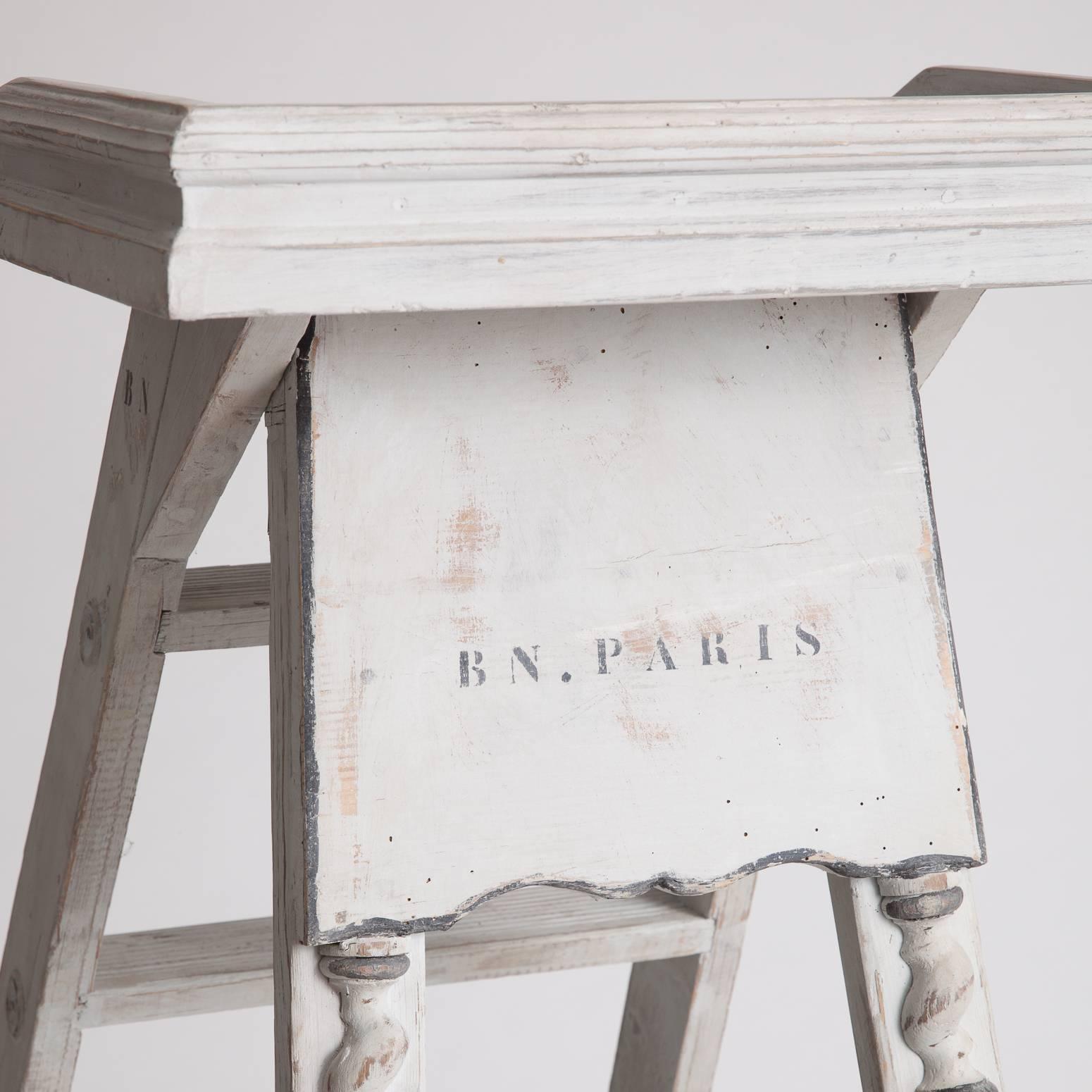 This wonderful old library ladder comes from a group of ladders that were deasessioned from the Bibliotheque National of Paris in the first half of the 20th century. With an old grey paint surface, a convenient top shelf for books, and applied