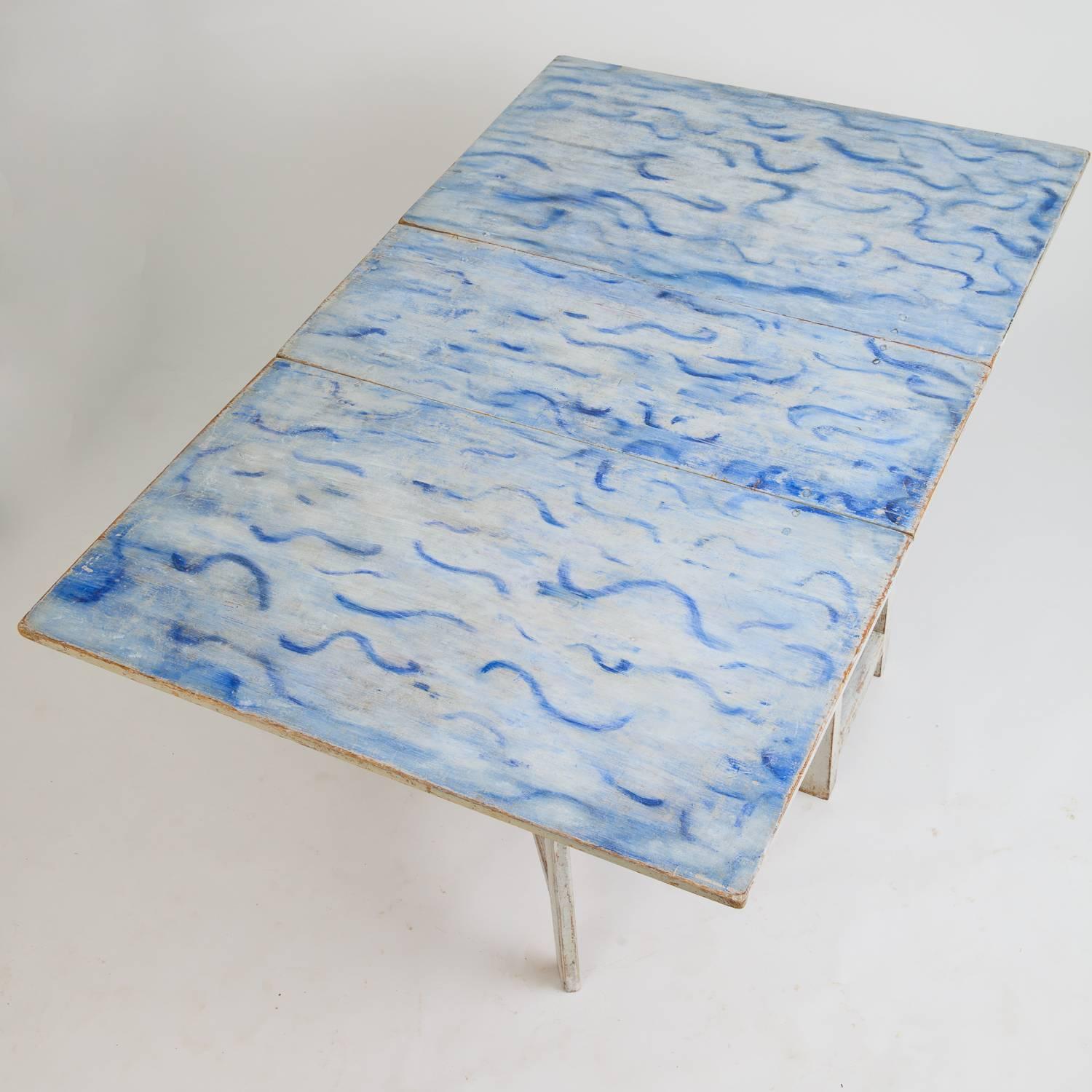 This fantastic Swedish drop-leaf table (slagbord) is a once in a lifetime piece with a beautiful original painted top surface with vibrant waves of blue against a white background. The base retains the original white paint and the leaves drop down