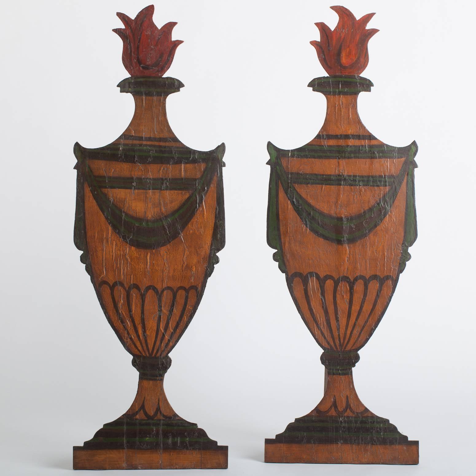 These painted wooden urns might have been part of a 19th century stage set depicting a fanciful garden. They have wooden back supports to display them at an angle but also have hangers allowing them to hang on a wall as a decorative element. There