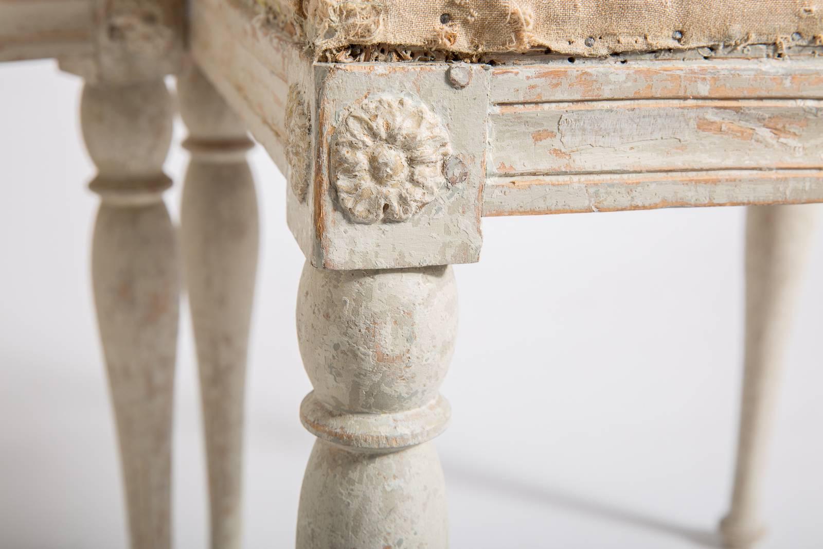 These Swedish Gustavian period stools retain the original pale grey paint surface. The apron has carved medallions on each corner that are typical of the period. The simple legs end in a pad foot. They have been recovered in a white French linen