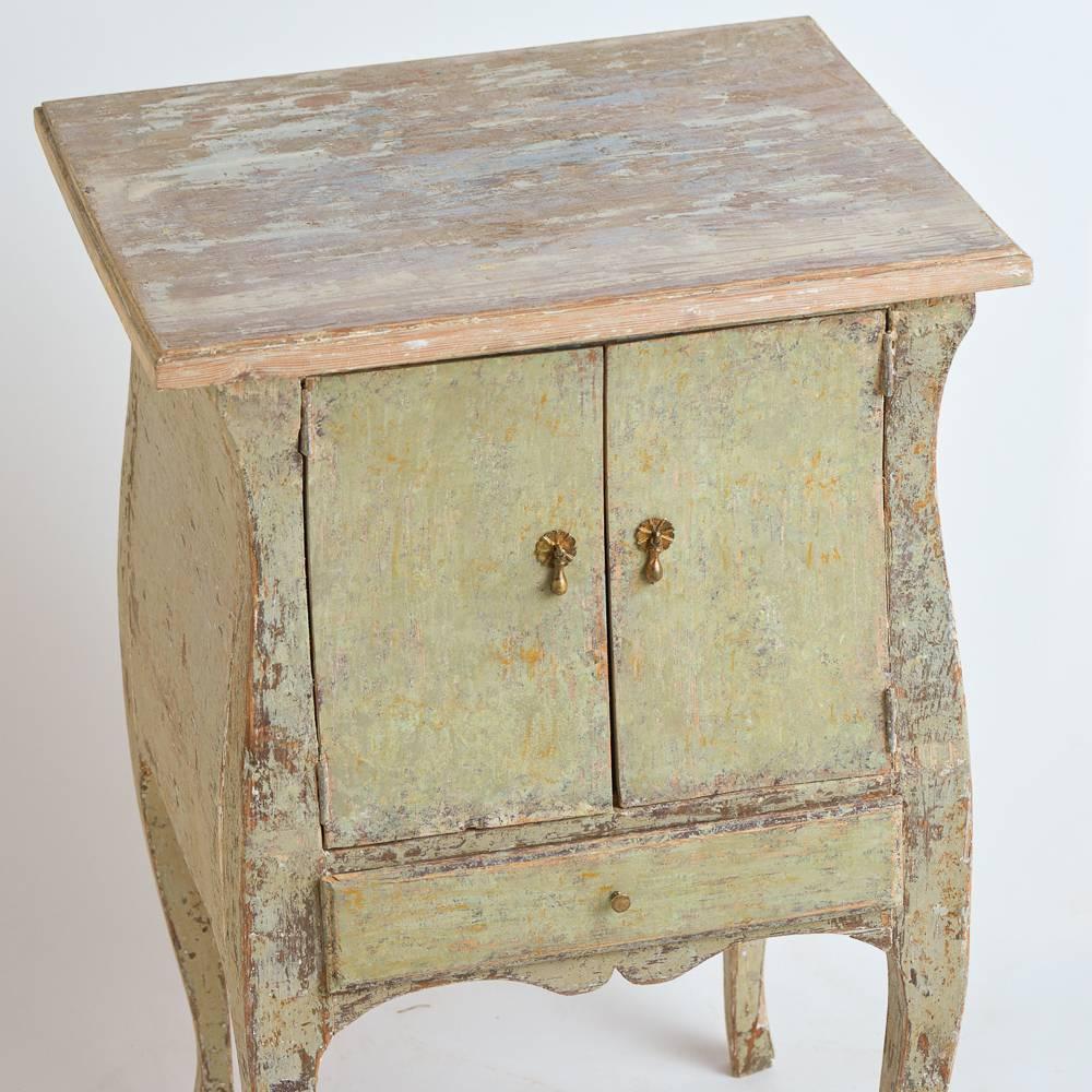 This charming cabinet is a very hard to find size that is perfect as a side table or bedside table. It retains the original pale green paint surface and has two doors opened by period appropriate pulls. The curved legs and body shape are typical of