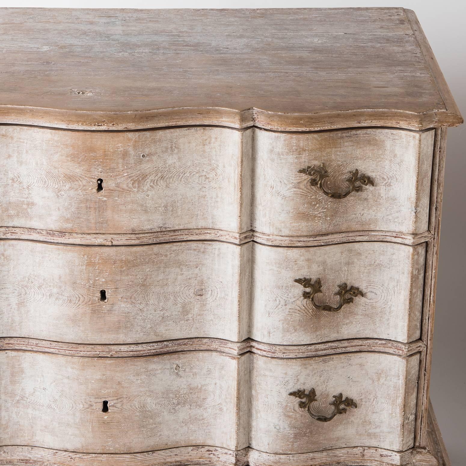 This important three-drawer chest with a graceful serpentine front sits on a separate base with slightly exaggerated curved legs which adds to it stature. The paint surface with touches of white paint remaining is all original. The hardware is