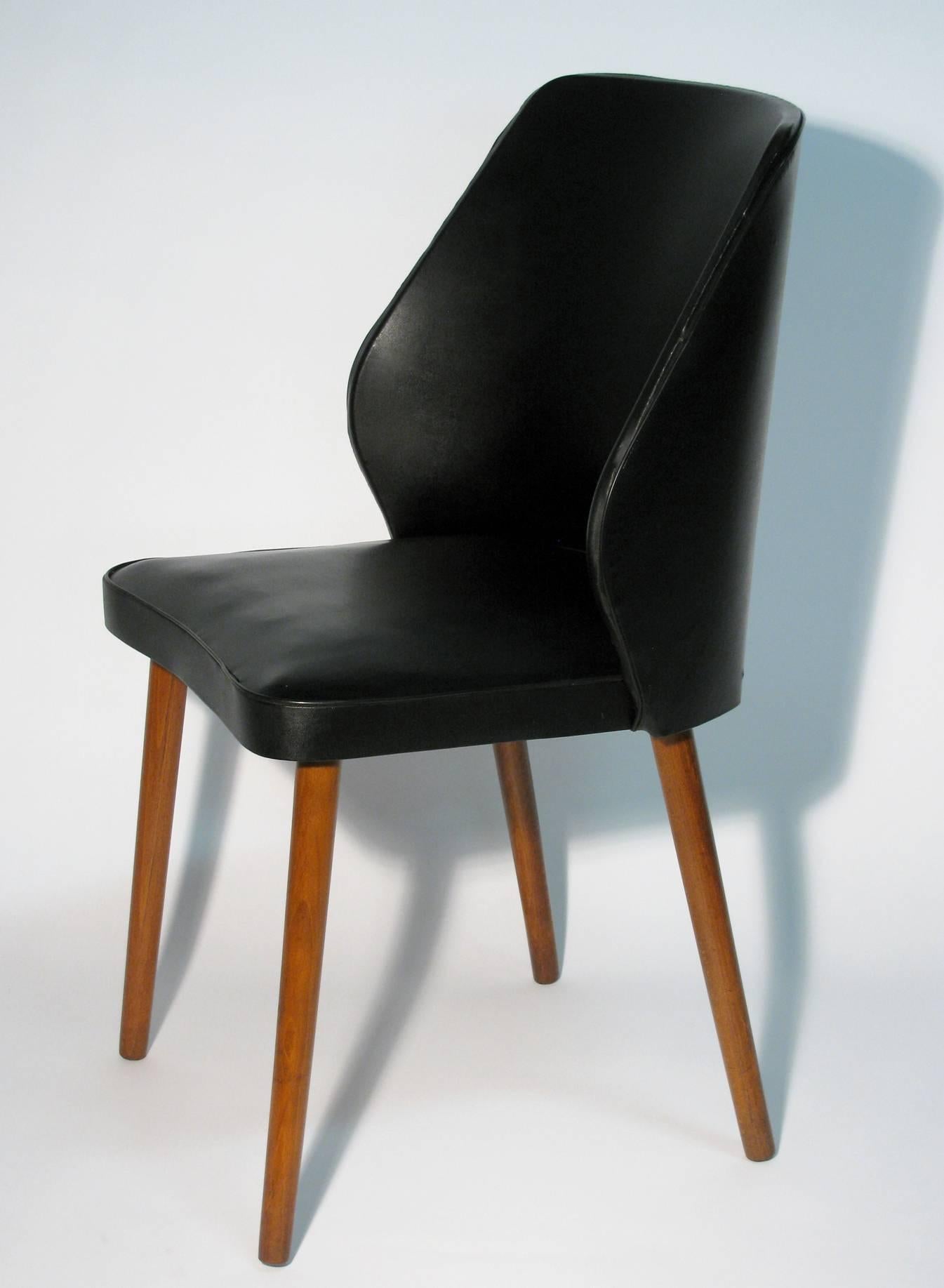Danish modern occasional chair of black pebble grain faux leather, with a curved back, serpentine-front seat, on tapered teak legs.
