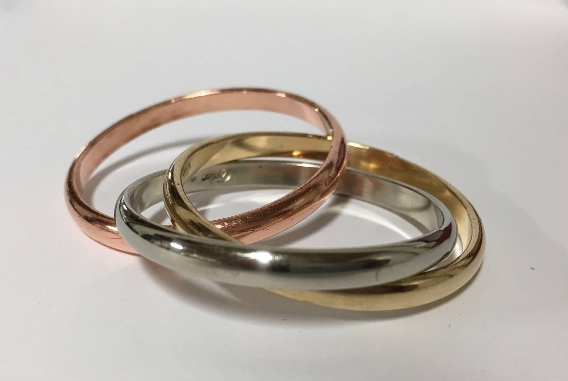 Set of four yellow, silver and rose gold-tone Cartier Trinity interlocking napkin rings. Includes original box. The rings have a diameter of 2.5 inches (each).