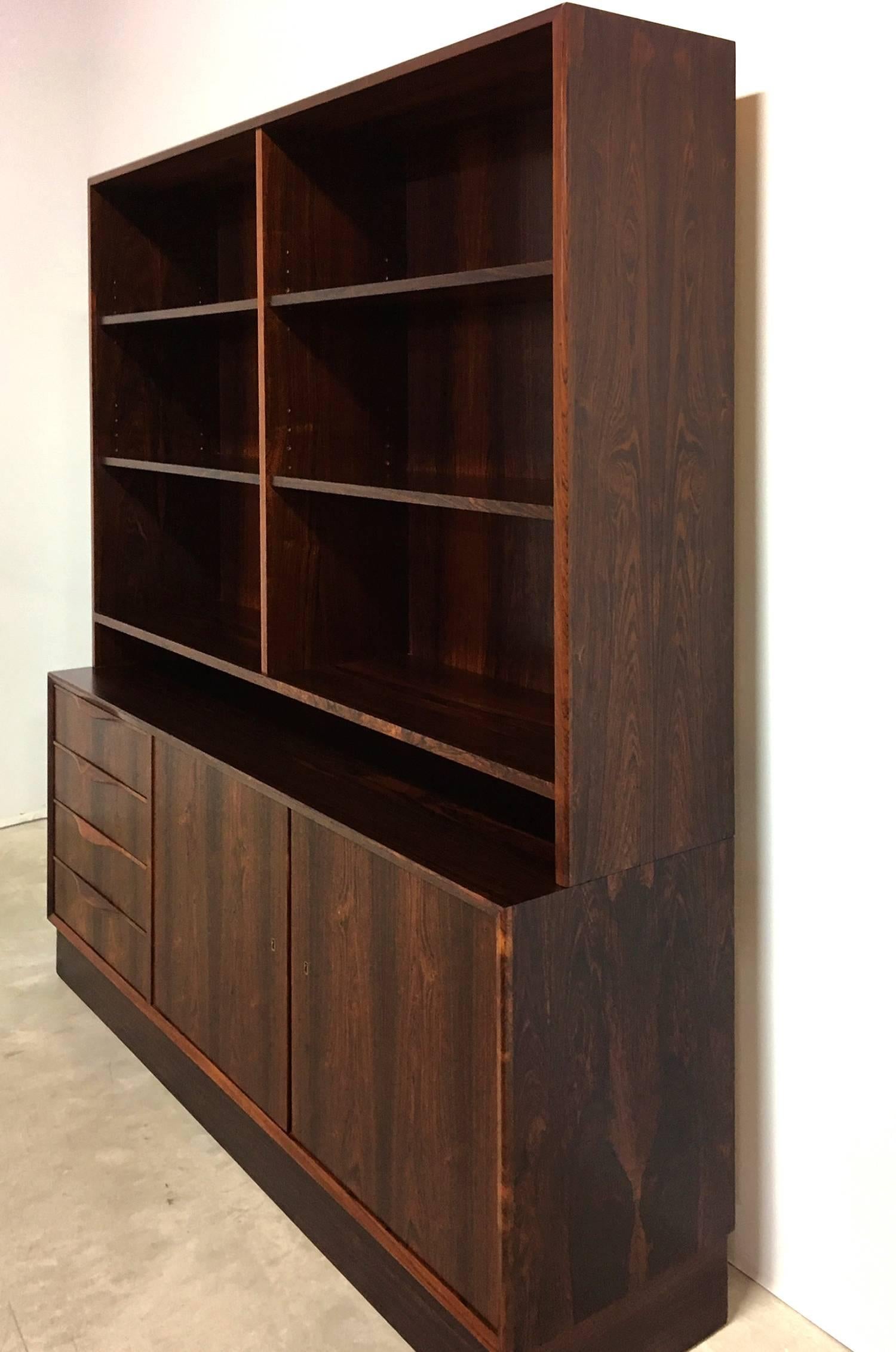Danish Mid-Century Modern bookcase cabinet of exotic rosewood. The rectangular upper case fitted with shelves that adjust, above the lower case with two doors, opening to shelved interior right half, and a bank of four drawers on the left side. The
