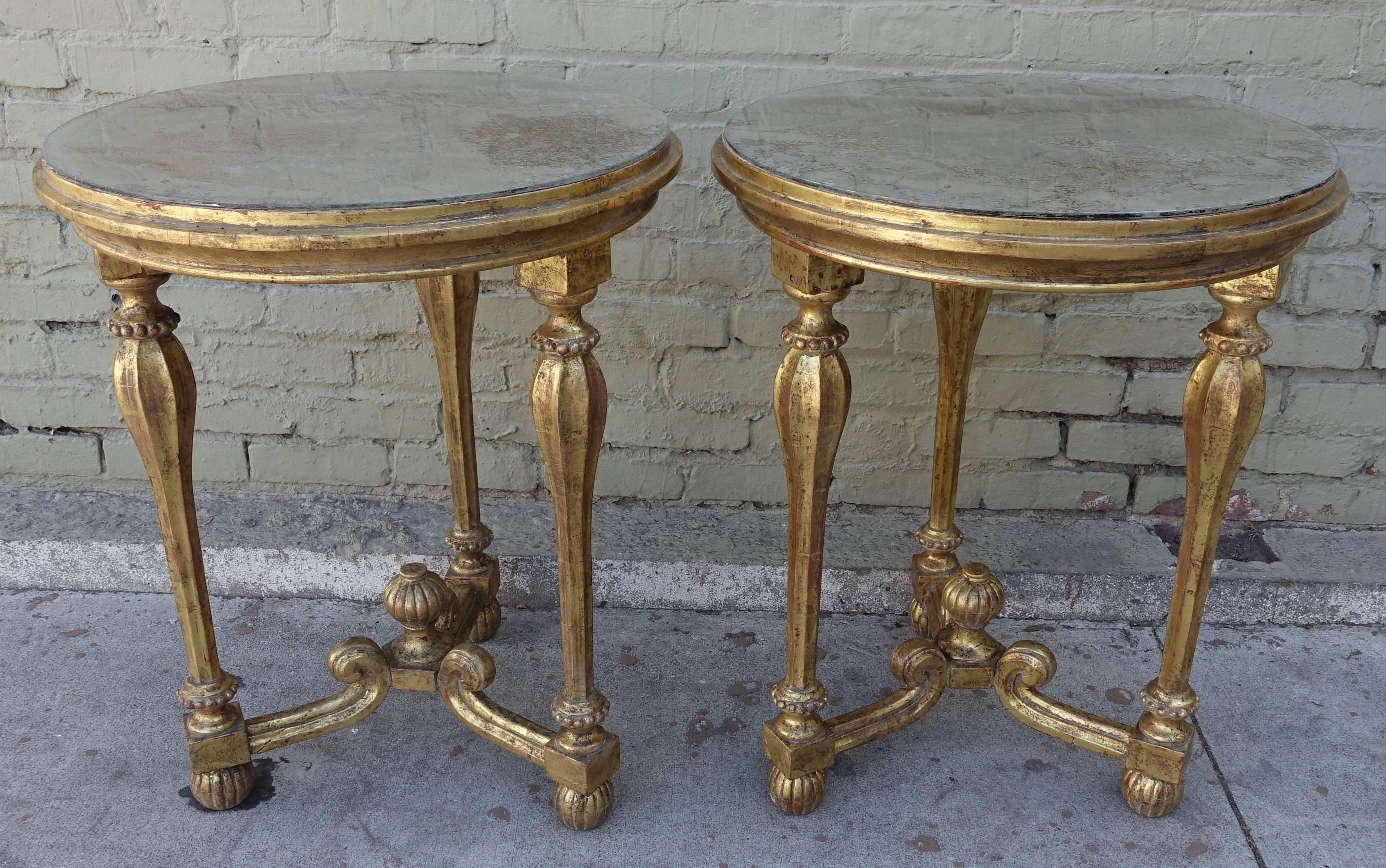 Pair of giltwood Italian tables standing on tripod bases and finished with antiqued mirrored tops. Bottom stretcher meets at center finial and the legs end in fluted bun feet.